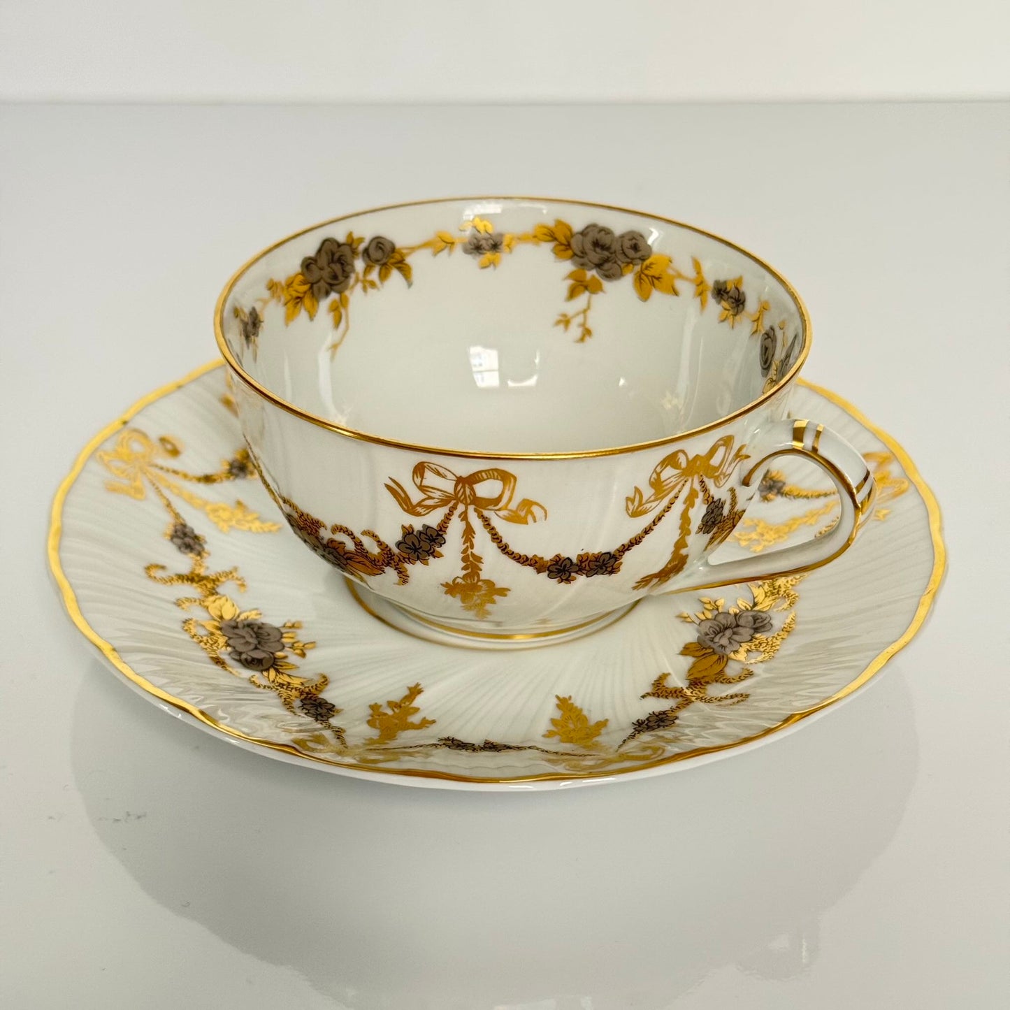 English: Pair of vintage Bernardaud Limoges tea cups and saucers with ribbon and floral garland motif, richly gilded and silvered porcelain set.; 日本語: ベルナルド リモージュ製ヴィンテージ ティーカップ&ソーサー2客セット、リボンと花のガーランド柄、金彩と銀彩装飾入りの磁器セット。; Français: Paire de tasses à thé et soucoupes vintage Bernardaud Limoges, décor de rubans/nœuds et guirlandes florales, ensemble en porcelaine richement dorée et argentée.