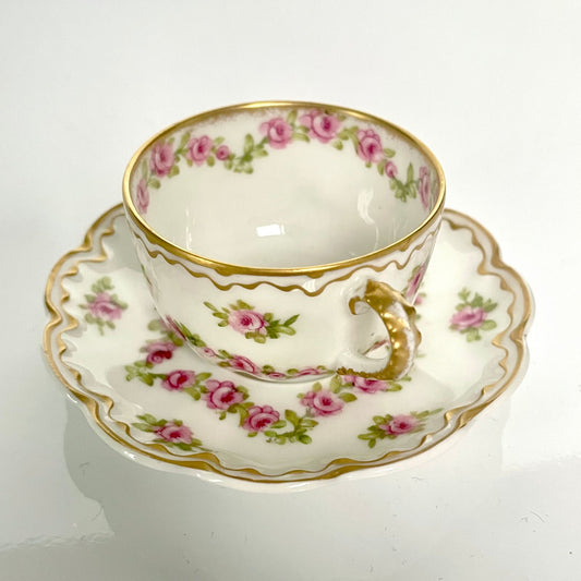 日本語: 優美なバラのガーランド模様のカップ&ソーサーセット。繊細な花柄が特徴で、裏面に「Grand Dépôt E. Bourgeois」の刻印あり。19世紀後期から20世紀初頭に製作された品。; English: Elegant cup and saucer set featuring a delicate garland of roses. Marked with "Grand Dépôt E. Bourgeois" on the underside. Produced in the late 19th to early 20th century. ; Français: Élégant ensemble tasse et soucoupe avec guirlande de roses délicate. Marqué "Grand Dépôt E. Bourgeois" au dos. Fabriqué entre la fin du 19ᵉ et le début du 20ᵉ siècle.