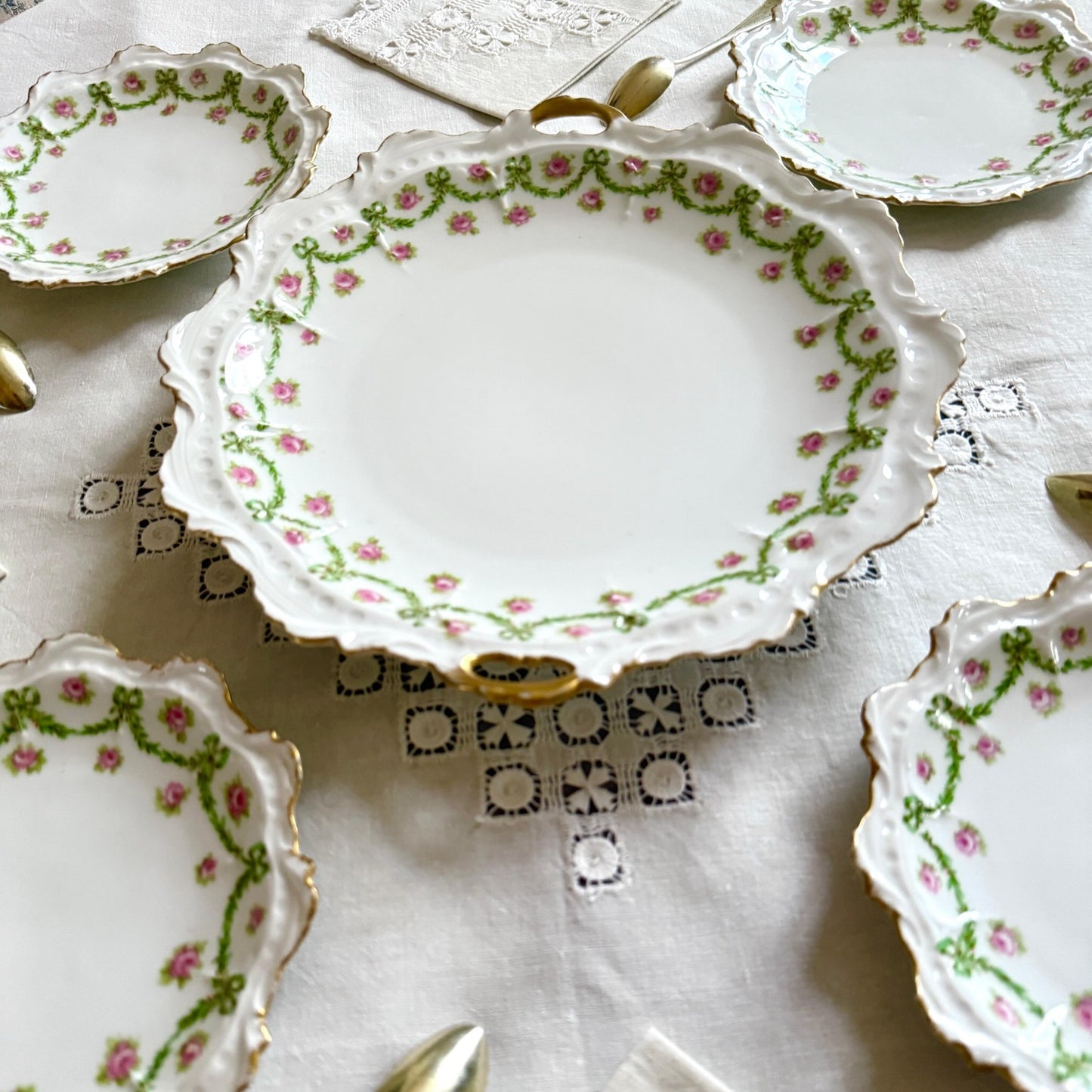 English: Limoges porcelain cake plate with scalloped edge, decorated with delicate ribbons and rose motifs in soft colors and gold accents; early 20th-century French design.; Français: Plat à gâteau en porcelaine de Limoges au bord ondulé, orné de motifs de rubans et de roses avec des touches dorées délicates ; design français du début du XXe siècle.; 日本語: リモージュ製の磁器ケーキ皿、波打つ縁と柔らかな色調のリボンとバラの装飾、繊細な金彩付き、20世紀初頭フランス製デザイン。
