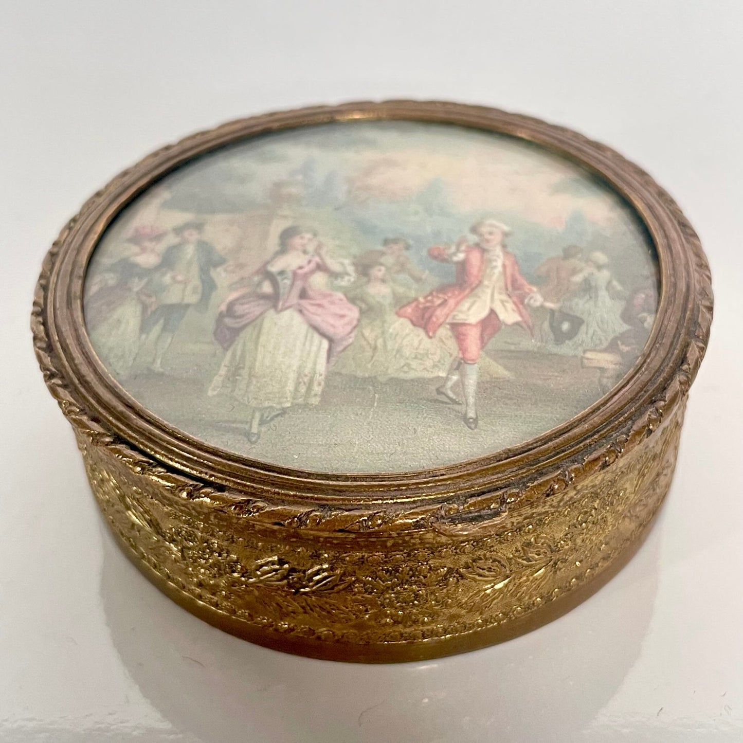日本語: ルイ16世様式のトリンケットボックス(小物入れ)。18世紀のフランス貴族の集い「フェット・ギャラント」のシーンが描かれ、ブロンズ製で花のモチーフが施されています。; English: Louis XVI style trinket box featuring a miniature scene of a Fête Galante, crafted in bronze with an elegant flower motif. ; Français: Boîte à bijoux de style Louis XVI avec une miniature représentant une scène de Fête Galante, en bronze et ornée d’un motif floral élégant.