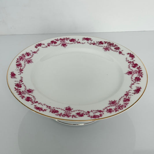 English: Antique Pirkenhammer porcelain cake stand decorated with ribbon and floral garland motif in pink and violet, early 20th century. ; Français : Présentoir à gâteau en porcelaine Pirkenhammer, décor de rubans et guirlandes florales rose/violet, début XXᵉ siècle. ; 日本語: ピルケンハンマー製アンティークケーキスタンド、ピンクパープルのリボンと花のガーランド装飾、20世紀初頭。