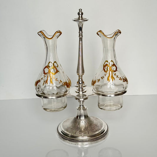 English: Silver plate cruet set by Armand Frénais, late 19th to early 20th century, with crystal bottles decorated with gilt ribbons and floral motifs; some wear and deformation to metal parts. ; 日本語: 19世紀末〜20世紀初頭、アルマン・フレネ製の銀メッキ製オイル&ビネガー入れセット。金彩リボンと花模様が施されたクリスタルボトル付き。金属部分にやや摩耗と歪みあり。; Français: Huilier vinaigrier en métal argenté par Armand Frénais, fin XIXe – début XXe siècle, flacons en cristal décorés de rubans et fleurs dorés ; quelques usures et déformations visibles sur le métal.