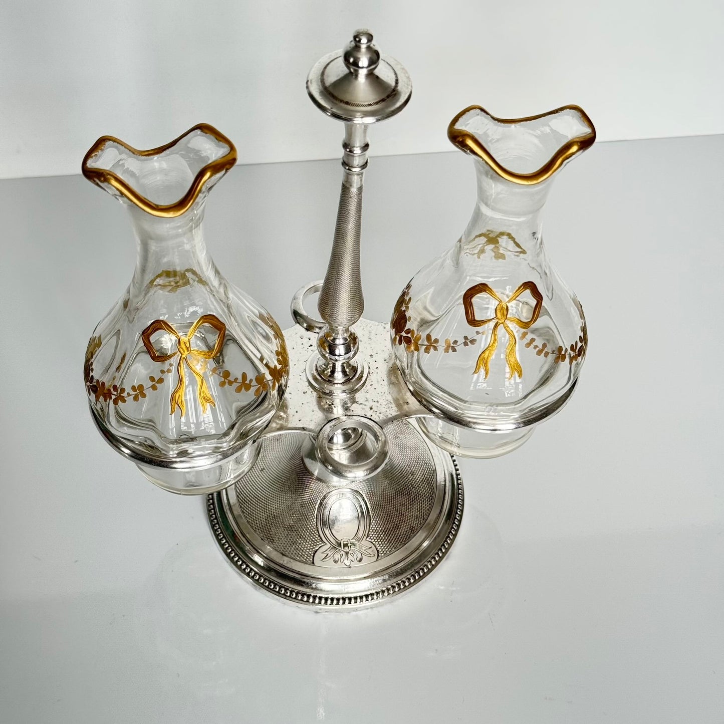 English: Silver plate cruet set by Armand Frénais, late 19th to early 20th century, with crystal bottles decorated with gilt ribbons and floral motifs; some wear and deformation to metal parts. ; 日本語: 19世紀末〜20世紀初頭、アルマン・フレネ製の銀メッキ製オイル&ビネガー入れセット。金彩リボンと花模様が施されたクリスタルボトル付き。金属部分にやや摩耗と歪みあり。; Français: Huilier vinaigrier en métal argenté par Armand Frénais, fin XIXe – début XXe siècle, flacons en cristal décorés de rubans et fleurs dorés ; quelques usures et déformations visibles sur le métal.
