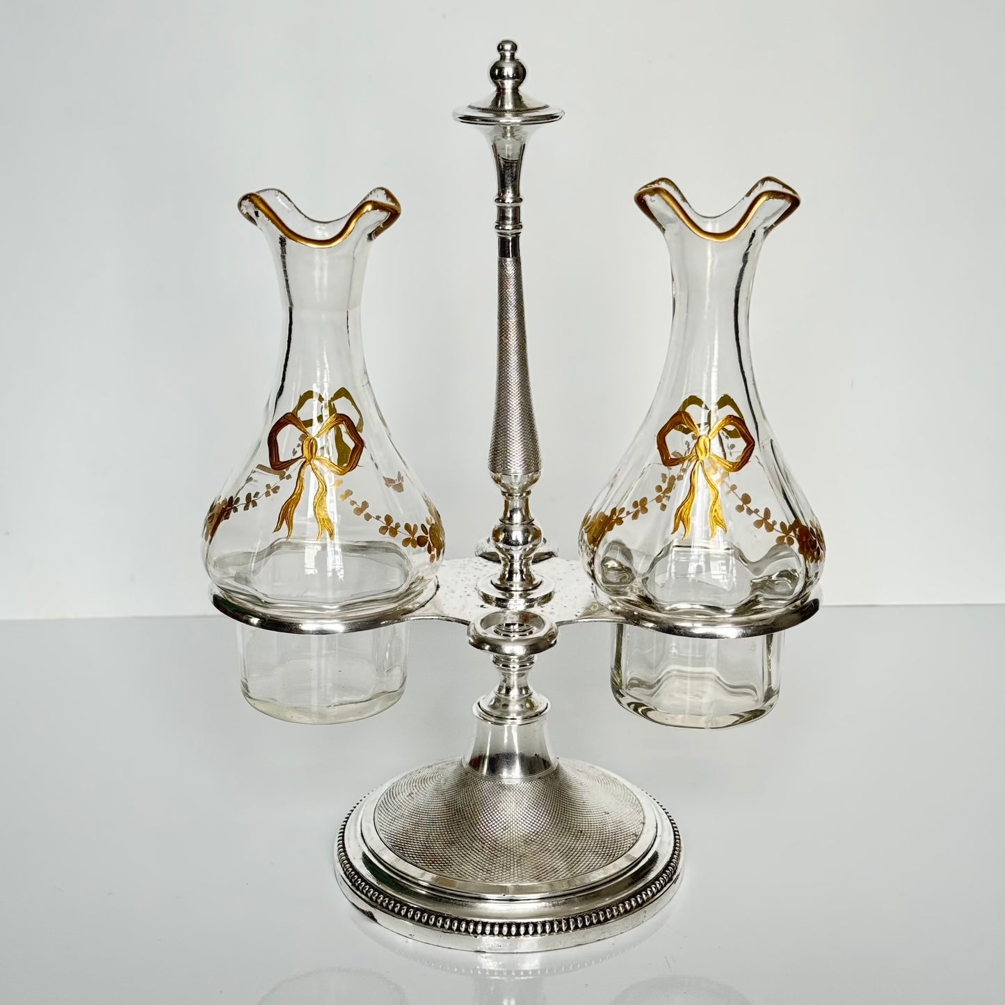 English: Silver plate cruet set by Armand Frénais, late 19th to early 20th century, with crystal bottles decorated with gilt ribbons and floral motifs; some wear and deformation to metal parts. ; 日本語: 19世紀末〜20世紀初頭、アルマン・フレネ製の銀メッキ製オイル&ビネガー入れセット。金彩リボンと花模様が施されたクリスタルボトル付き。金属部分にやや摩耗と歪みあり。; Français: Huilier vinaigrier en métal argenté par Armand Frénais, fin XIXe – début XXe siècle, flacons en cristal décorés de rubans et fleurs dorés ; quelques usures et déformations visibles sur le métal.