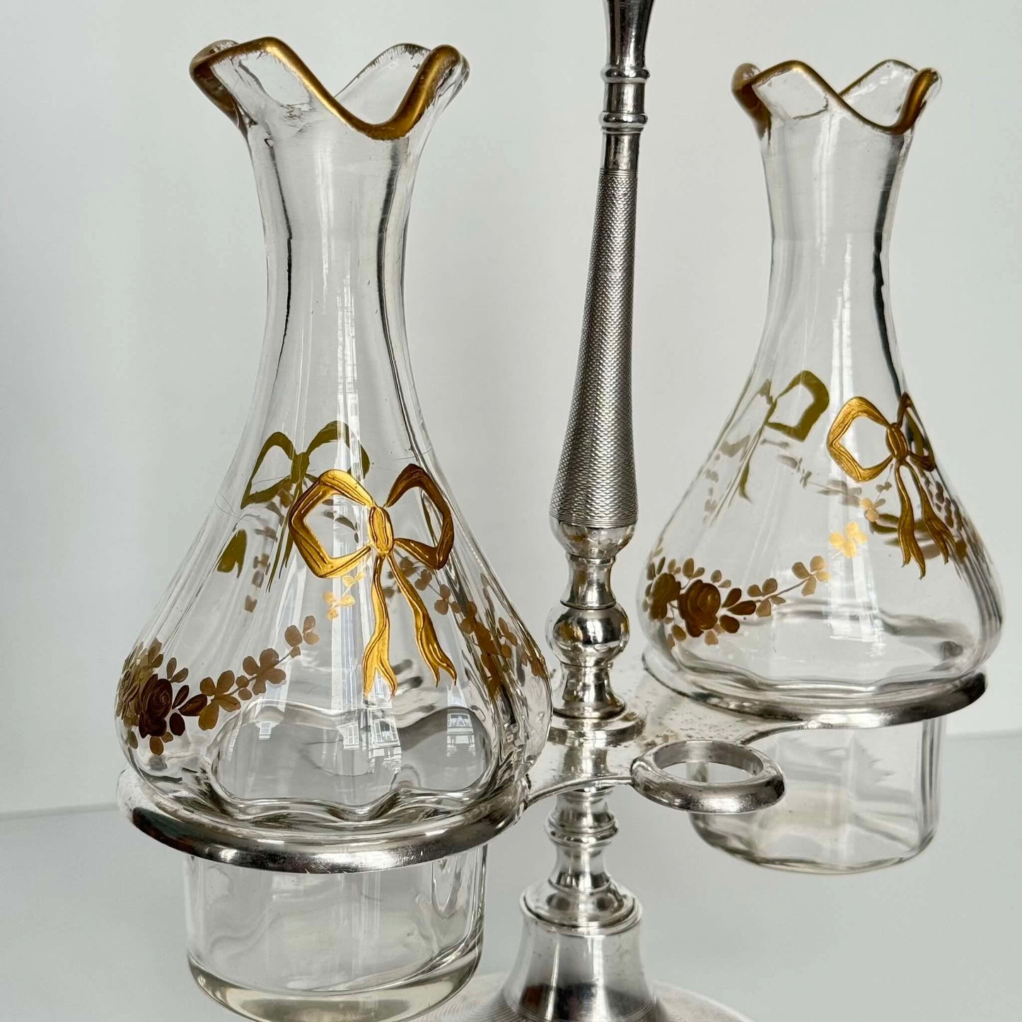 English: Silver plate cruet set by Armand Frénais, late 19th to early 20th century, with crystal bottles decorated with gilt ribbons and floral motifs; some wear and deformation to metal parts. ; 日本語: 19世紀末〜20世紀初頭、アルマン・フレネ製の銀メッキ製オイル&ビネガー入れセット。金彩リボンと花模様が施されたクリスタルボトル付き。金属部分にやや摩耗と歪みあり。; Français: Huilier vinaigrier en métal argenté par Armand Frénais, fin XIXe – début XXe siècle, flacons en cristal décorés de rubans et fleurs dorés ; quelques usures et déformations visibles sur le métal.