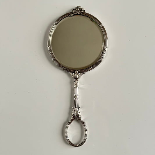 English: Silver plate hand mirror in Louis XVI style with crossed ribbons and decorative bow, late 19th to early 20th century, double-sided mirror ; 日本語: ルイ16世様式の銀メッキ手鏡、リボンと装飾的な結び目付き、19世紀末~20世紀初頭、両面鏡 ; Français: Miroir à main en métal argenté style Louis XVI avec rubans croisés et nœud, fin XIXe – début XXe siècle, miroir double face.