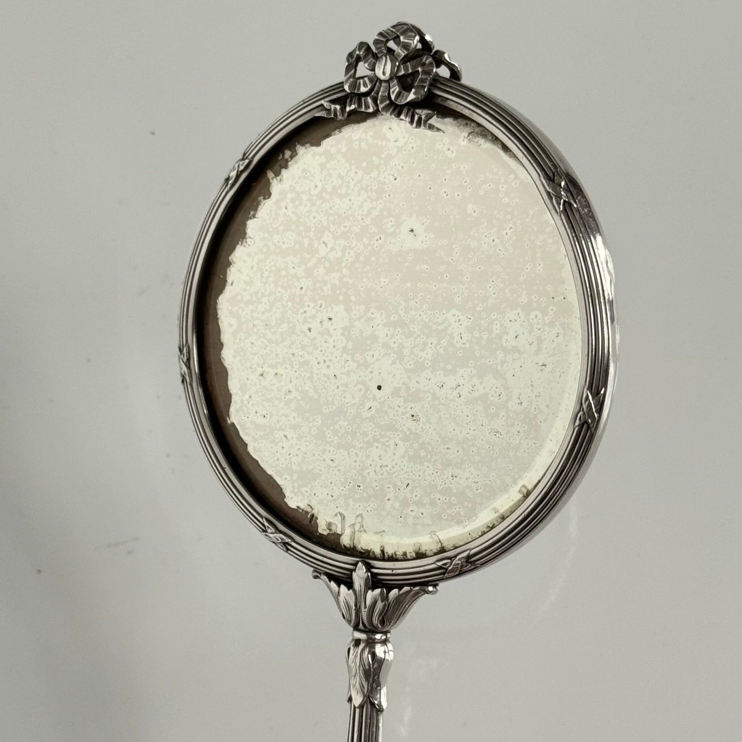 English: Silver plate hand mirror in Louis XVI style with crossed ribbons and decorative bow, late 19th to early 20th century, double-sided mirror ; 日本語: ルイ16世様式の銀メッキ手鏡、リボンと装飾的な結び目付き、19世紀末~20世紀初頭、両面鏡 ; Français: Miroir à main en métal argenté style Louis XVI avec rubans croisés et nœud, fin XIXe – début XXe siècle, miroir double face.
