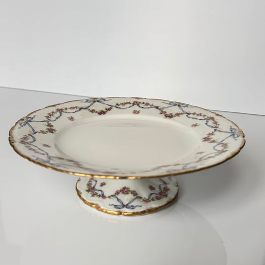 日本語: アビランド製リモージュ磁器のケーキスタンド。バラのガーランド、リボンモチーフ、金彩の縁取りが特徴。18世紀後期フランス様式に着想を得て製作。; English: Haviland Limoges porcelain cake stand with rose garlands, ribbon motifs, and gold trim. Inspired by late 18th-century French style.; Français: Présentoir à gâteau en porcelaine Haviland Limoges, guirlandes de roses, rubans et bordure dorée. Inspiré du style français fin XVIIIᵉ siècle.