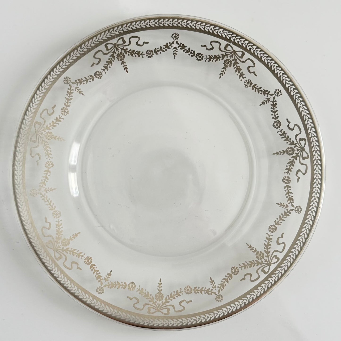 English: Vintage glass dessert plate with silvered ribbon and garland design, elegant and lightly worn. ; Français : Assiette à dessert en verre vintage avec décor argenté de rubans et guirlandes, élégante et en très bon état. ; 日本語: 銀彩のリボンとガーランド模様が施されたヴィンテージのガラス製デザートプレート。上品な印象でコンディション良好。