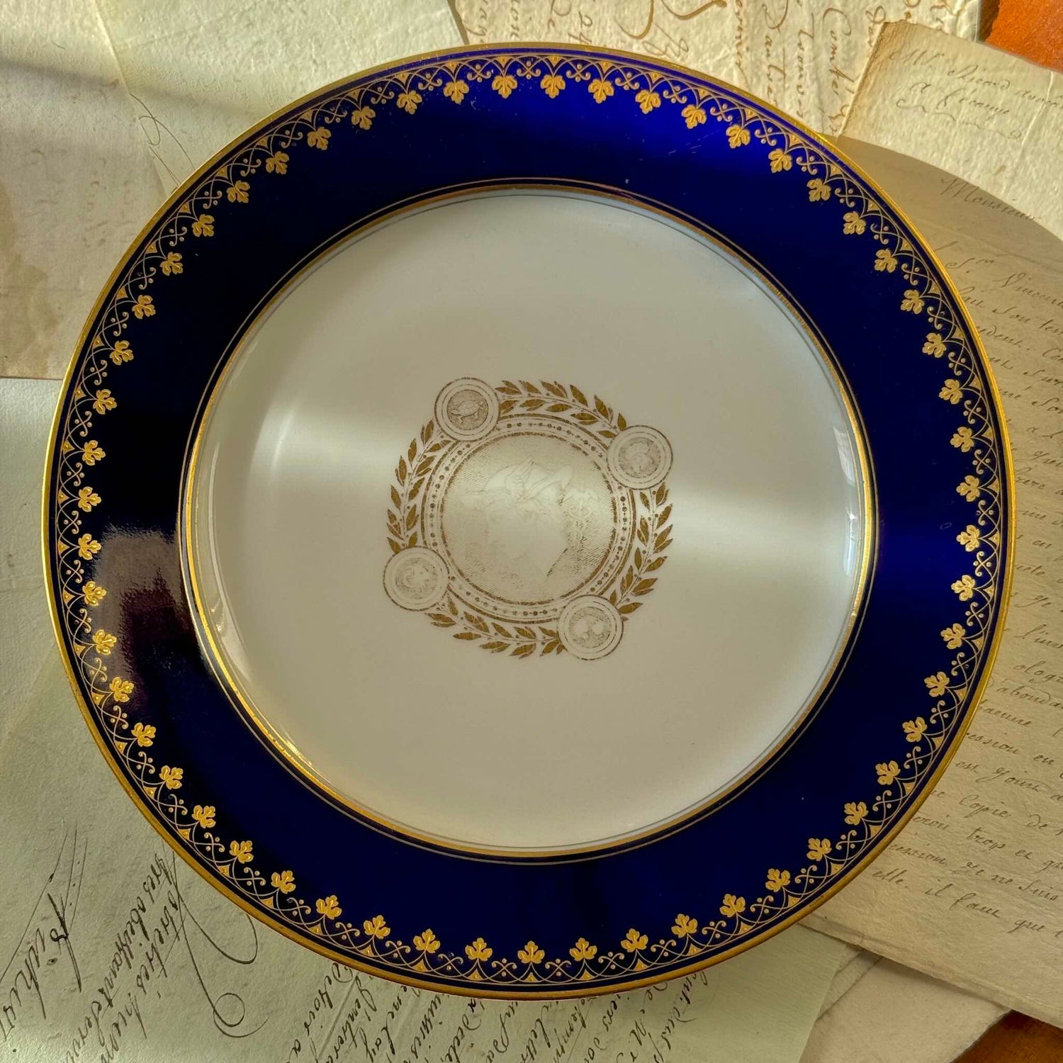 English: Sèvres porcelain plate, neoclassical style, with cobalt-blue border and gilded motifs of Mercury, laurel leaves, and symbolic animals, 1882–1883; 日本語: セーヴル製磁器プレート、新古典主義様式、コバルトブルーの縁に金彩装飾、メルクリウスと象徴的な動物、1882–1883年; Français: Assiette en porcelaine de Sèvres, style néoclassique, bordure bleu de Sèvres et motifs dorés de Mercure, laurier et animaux symboliques, 1882–1883.