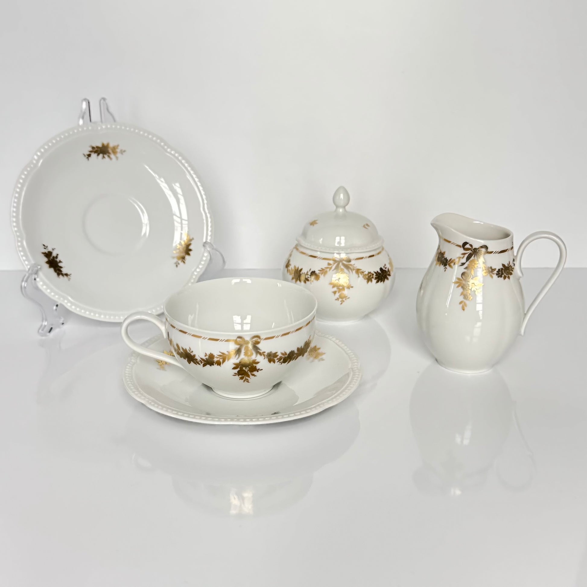 English: Vintage Bavaria “H&Co Selb” egoïste tea set with tea cup, two saucers, creamer, and sugar bowl, decorated with gilded bows and garlands. ; Français : Service à thé égoïste vintage Bavaria “H&Co Selb” comprenant tasse, 2 sous-tasses, pot à lait et sucrier, décoré de nœuds et guirlandes dorés. ; 日本語: ヴィンテージ ババリア「H&Co Selb」エゴイスト ティーセット（ティーカップ、ソーサー2枚、クリーマー、シュガーボウル）、金彩のリボンとガーランド装飾付き。