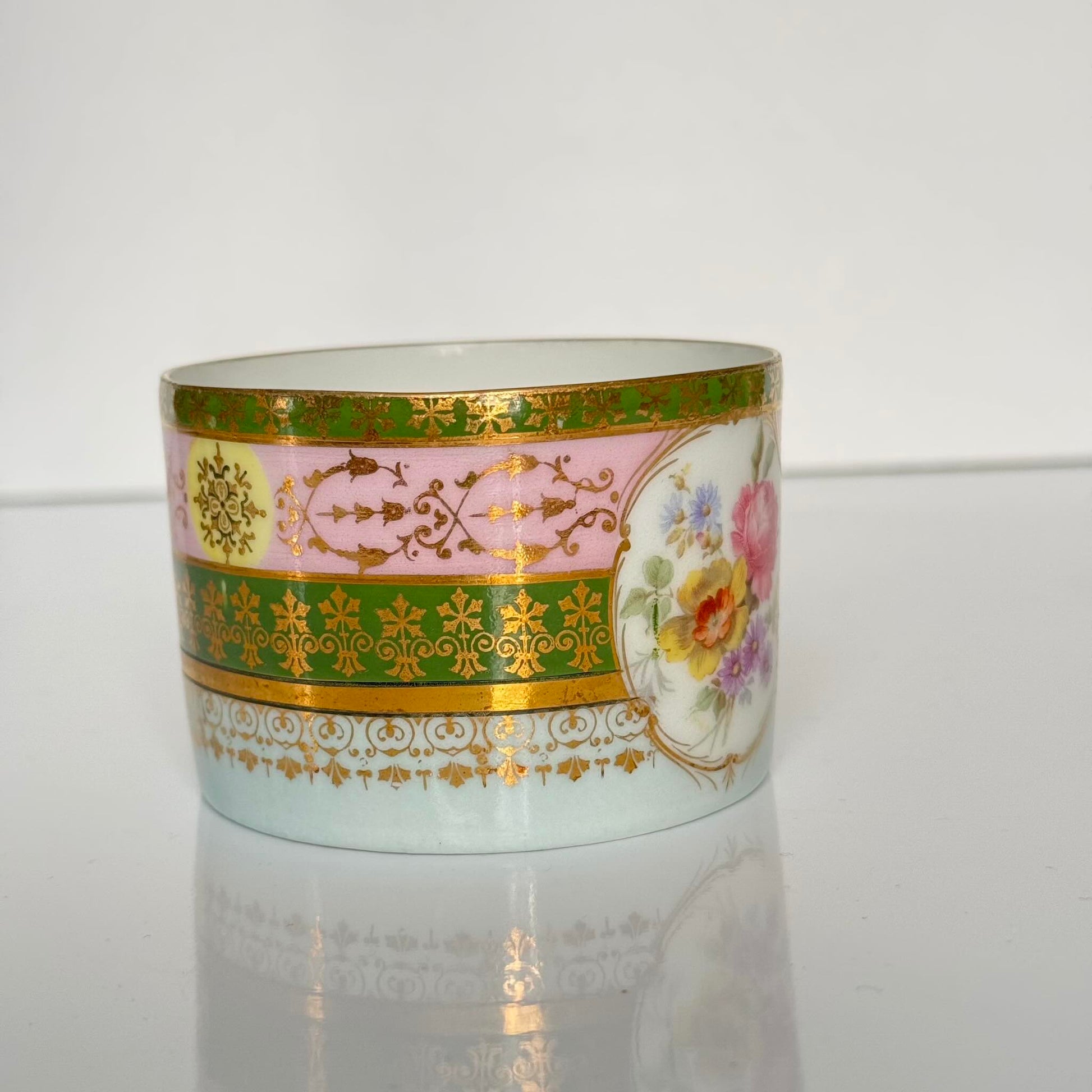 Porcelain cup and saucer set inspired by 18th-century Sèvres style, with delicate pink and green hues and gilded details.