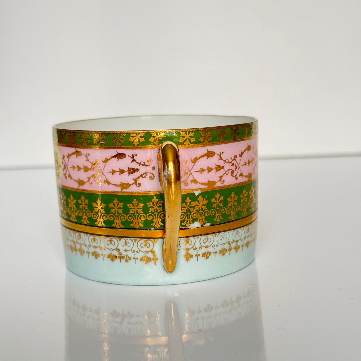 Porcelain cup and saucer set inspired by 18th-century Sèvres style, with delicate pink and green hues and gilded details.