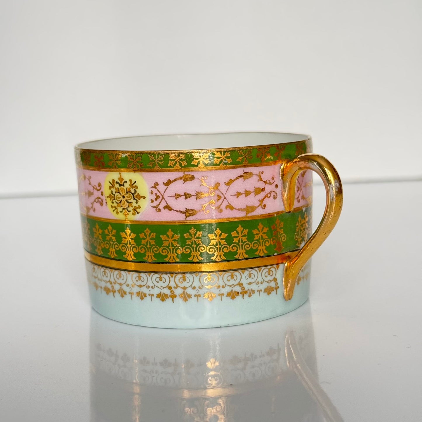 Porcelain cup and saucer set inspired by 18th-century Sèvres style, with delicate pink and green hues and gilded details.