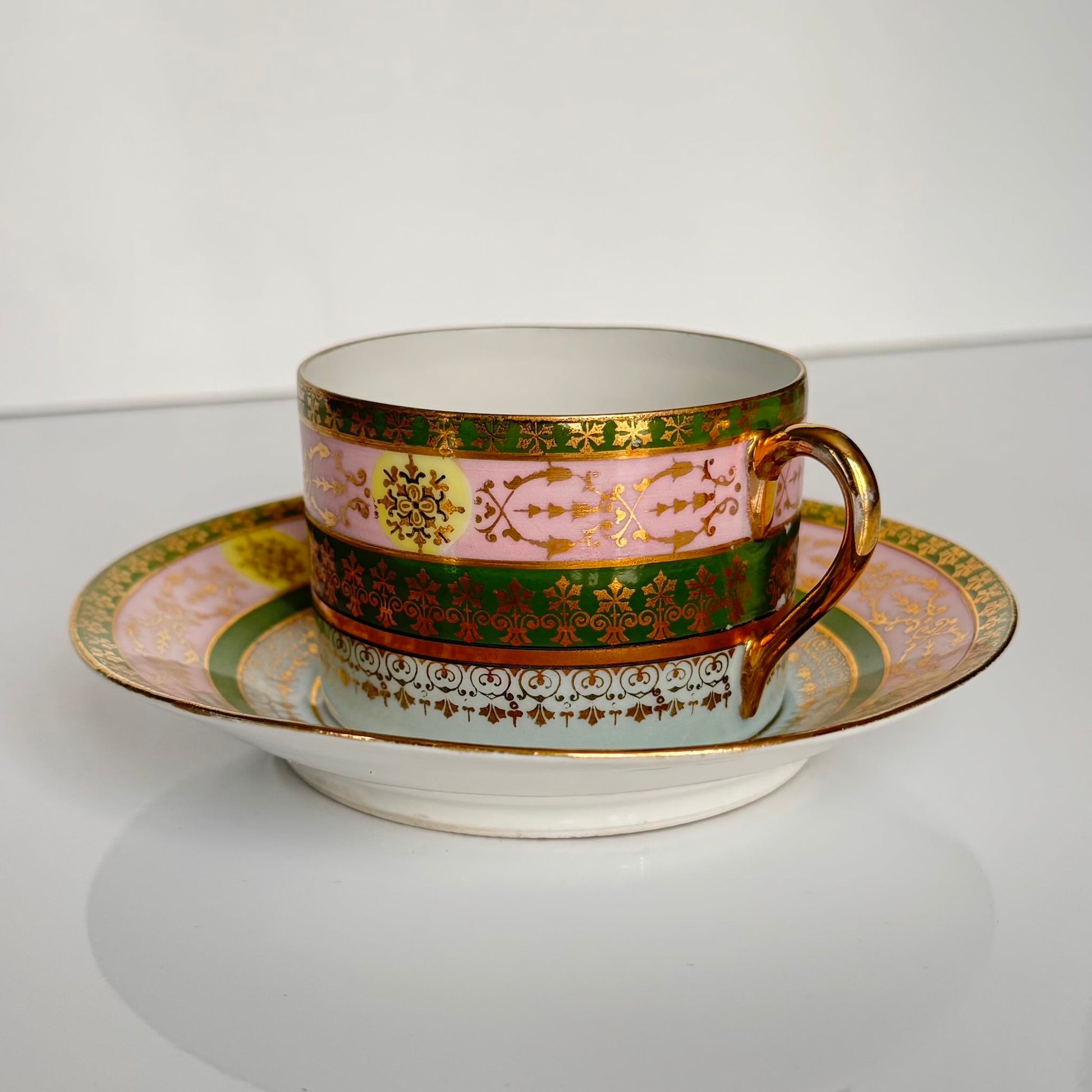 Porcelain cup and saucer set inspired by 18th-century Sèvres style, with delicate pink and green hues and gilded details.