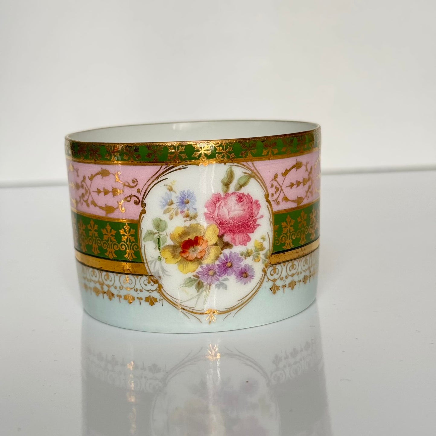 Porcelain cup and saucer set inspired by 18th-century Sèvres style, with delicate pink and green hues and gilded details.