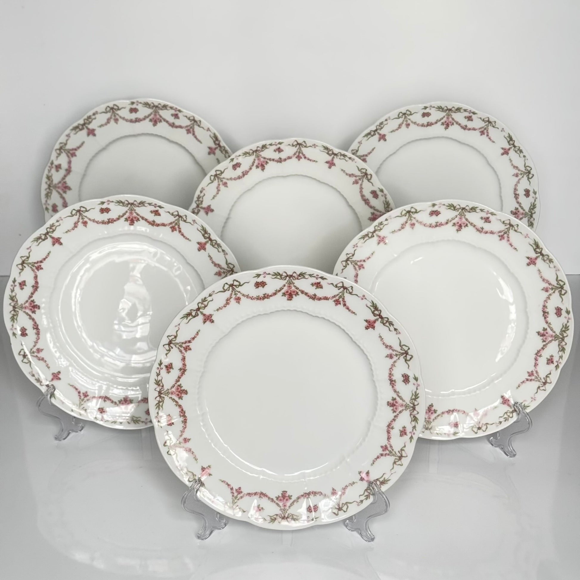 Set of two antique Limoges porcelain dessert plates by Ahrenfeldt, decorated with ribbon motifs and floral garlands, late 19th to early 20th century.