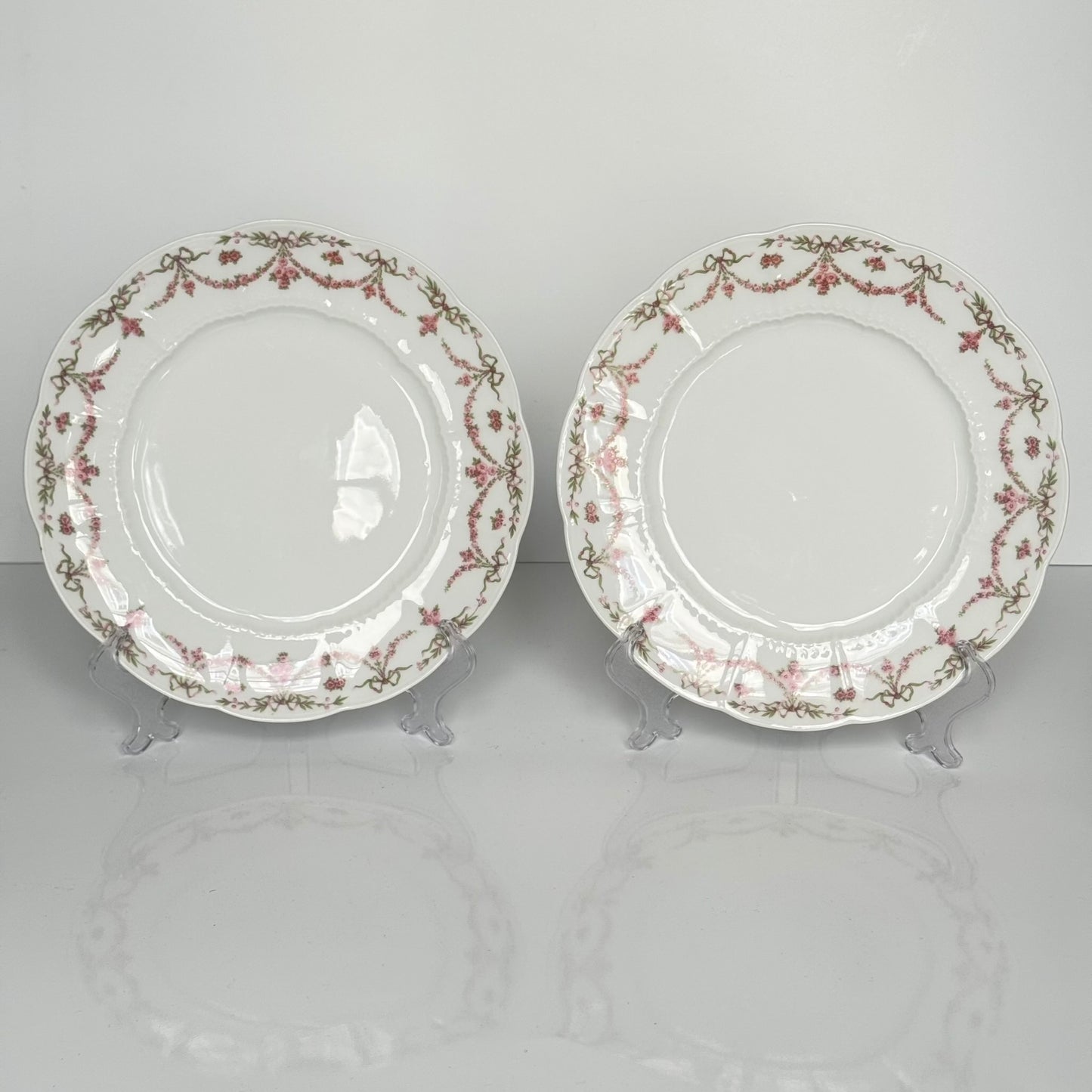 Set of two antique Limoges porcelain dessert plates by Ahrenfeldt, decorated with ribbon motifs and floral garlands, late 19th to early 20th century.