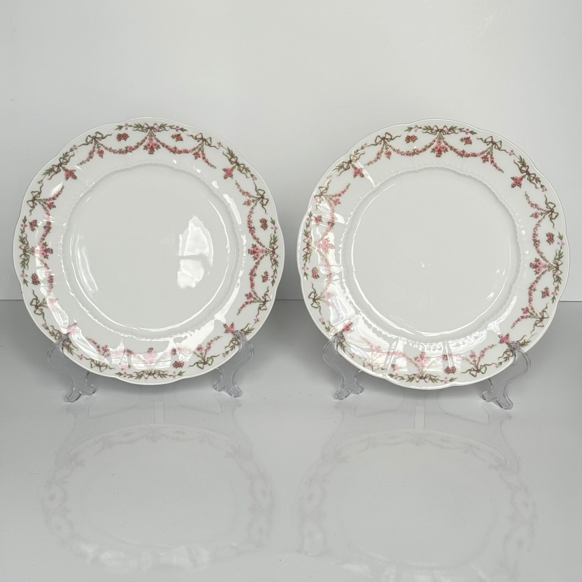 Set of two antique Limoges porcelain dessert plates by Ahrenfeldt, decorated with ribbon motifs and floral garlands, late 19th to early 20th century.