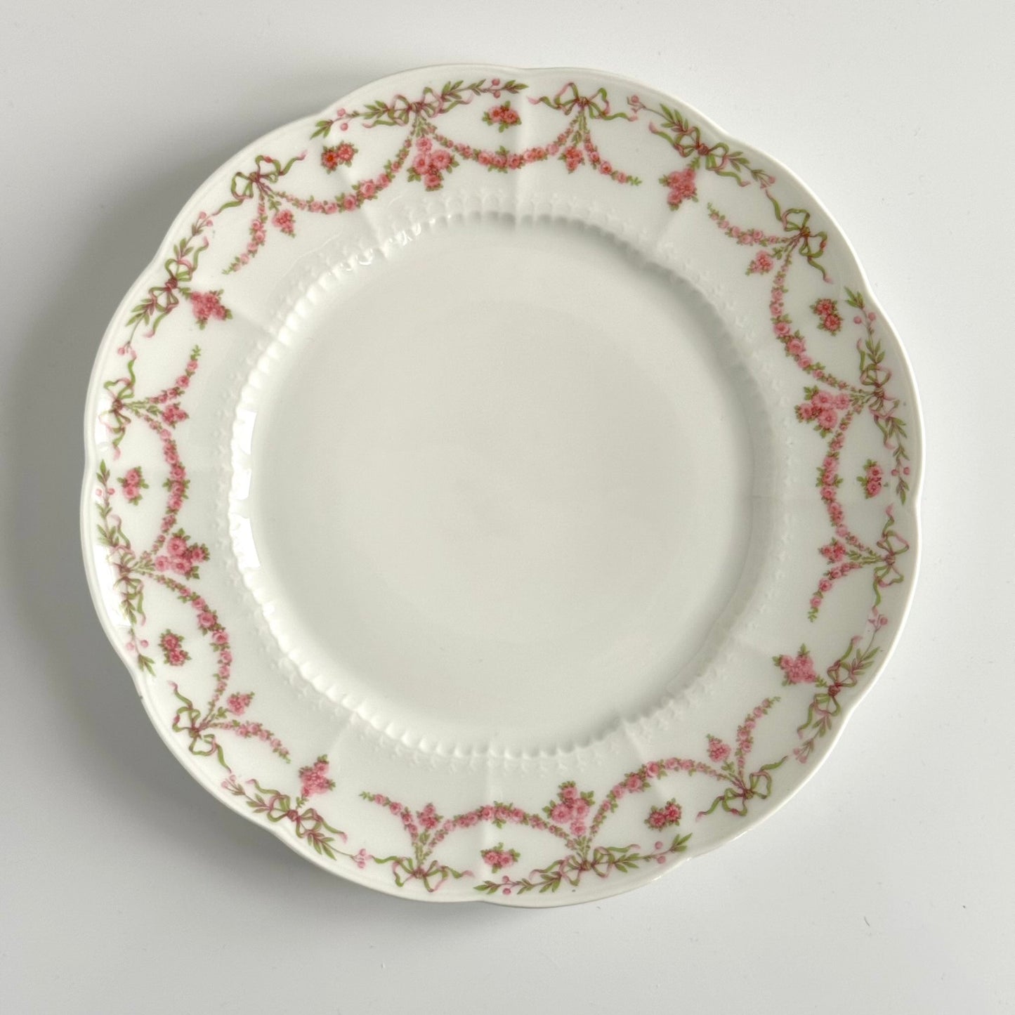 Set of two antique Limoges porcelain dessert plates by Ahrenfeldt, decorated with ribbon motifs and floral garlands, late 19th to early 20th century.