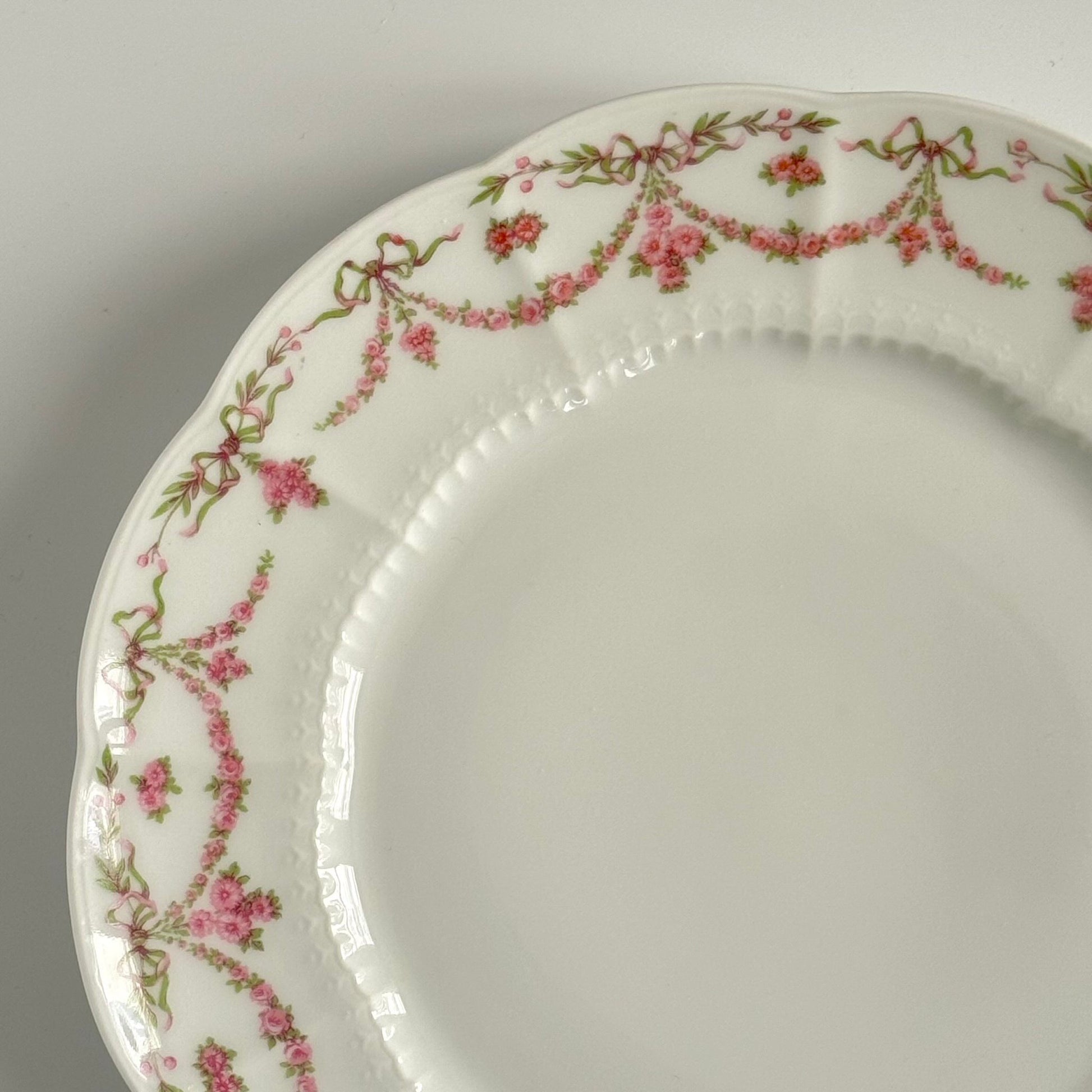 Set of two antique Limoges porcelain dessert plates by Ahrenfeldt, decorated with ribbon motifs and floral garlands, late 19th to early 20th century.