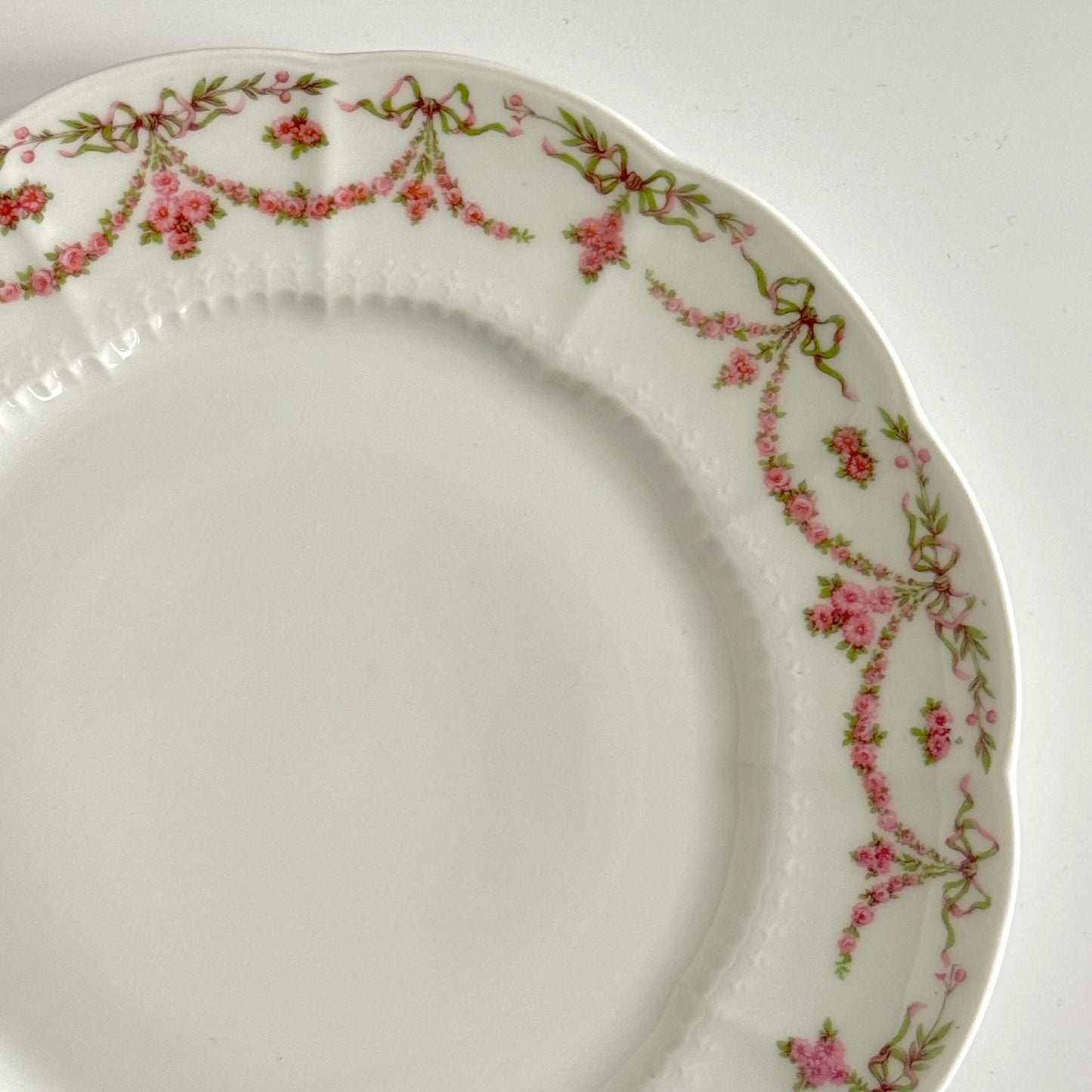 Set of two antique Limoges porcelain dessert plates by Ahrenfeldt, decorated with ribbon motifs and floral garlands, late 19th to early 20th century.