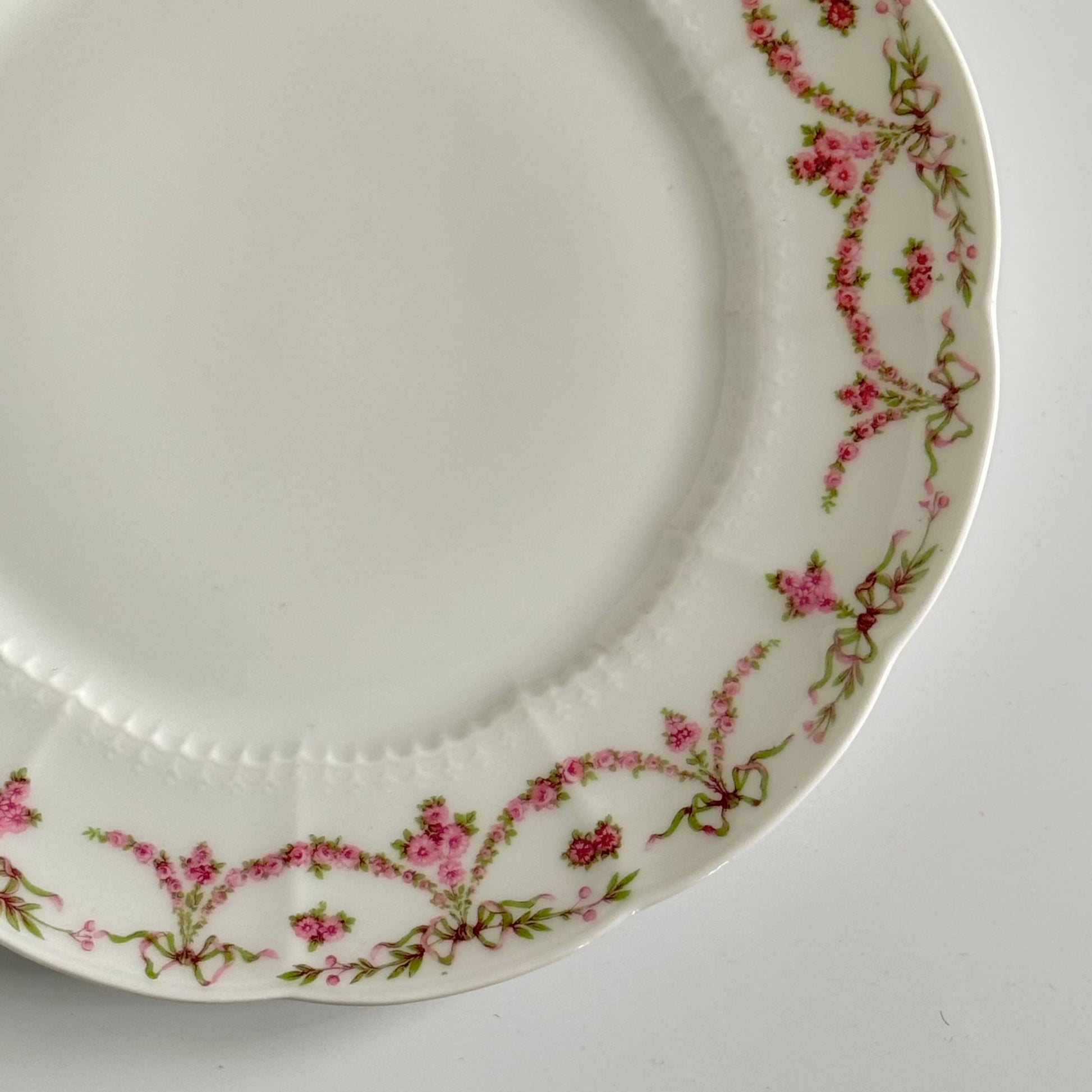 Set of two antique Limoges porcelain dessert plates by Ahrenfeldt, decorated with ribbon motifs and floral garlands, late 19th to early 20th century.