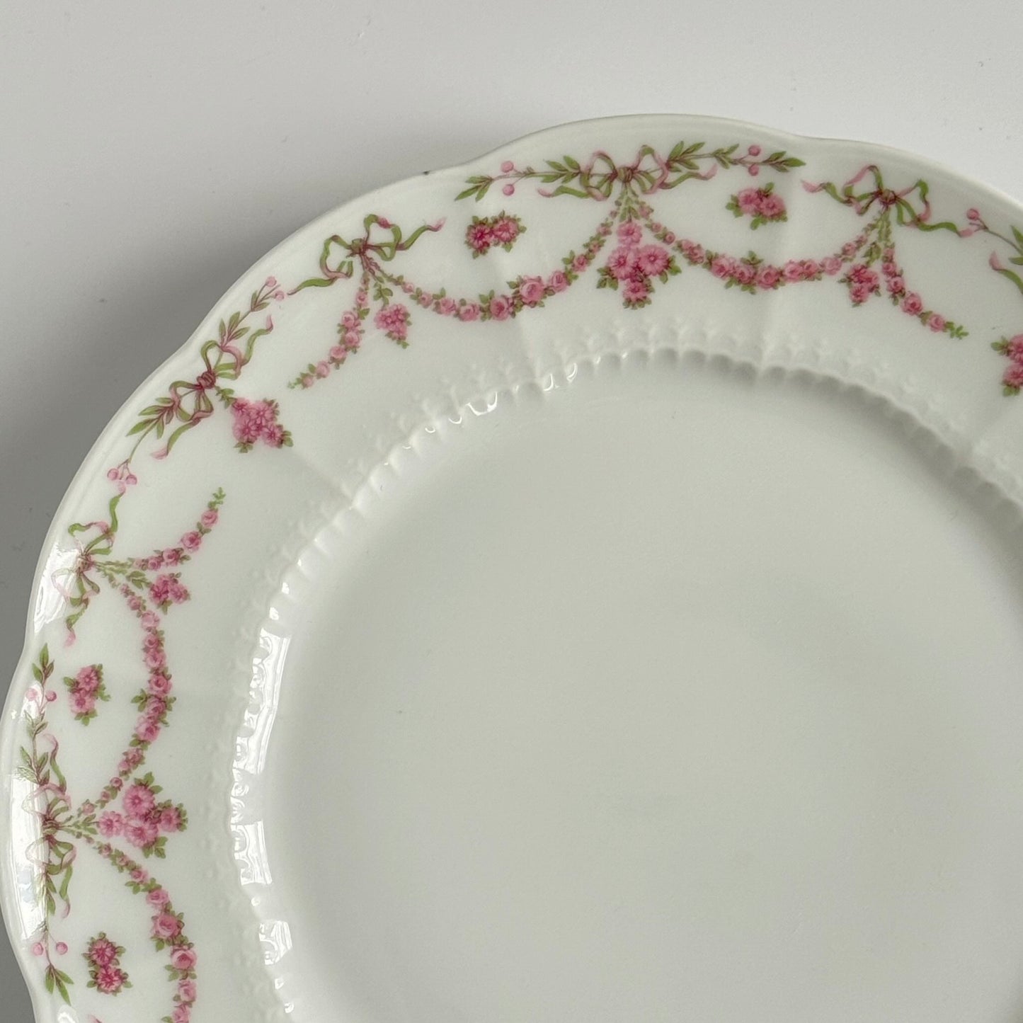 Set of two antique Limoges porcelain dessert plates by Ahrenfeldt, decorated with ribbon motifs and floral garlands, late 19th to early 20th century.