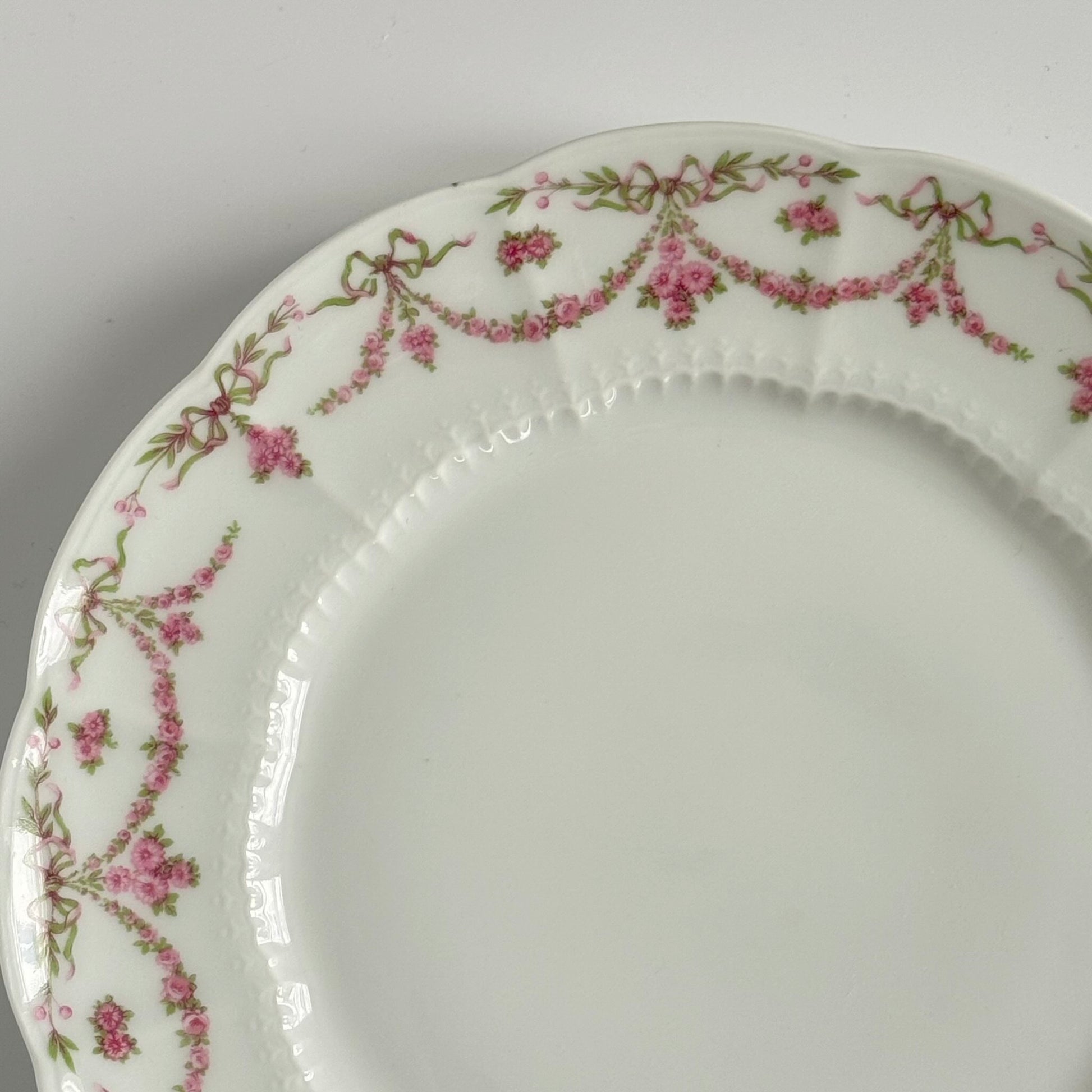 Set of two antique Limoges porcelain dessert plates by Ahrenfeldt, decorated with ribbon motifs and floral garlands, late 19th to early 20th century.