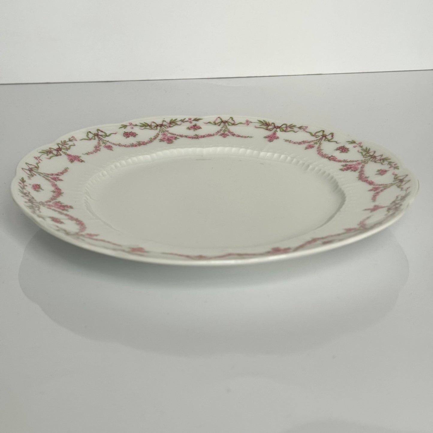 Set of two antique Limoges porcelain dessert plates by Ahrenfeldt, decorated with ribbon motifs and floral garlands, late 19th to early 20th century.