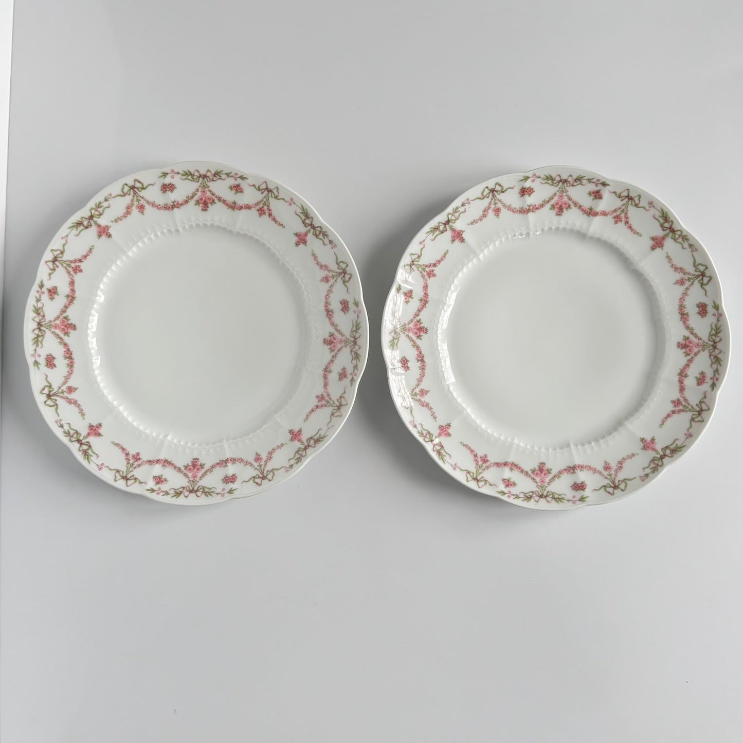 Set of two antique Limoges porcelain dessert plates by Ahrenfeldt, decorated with ribbon motifs and floral garlands, late 19th to early 20th century.