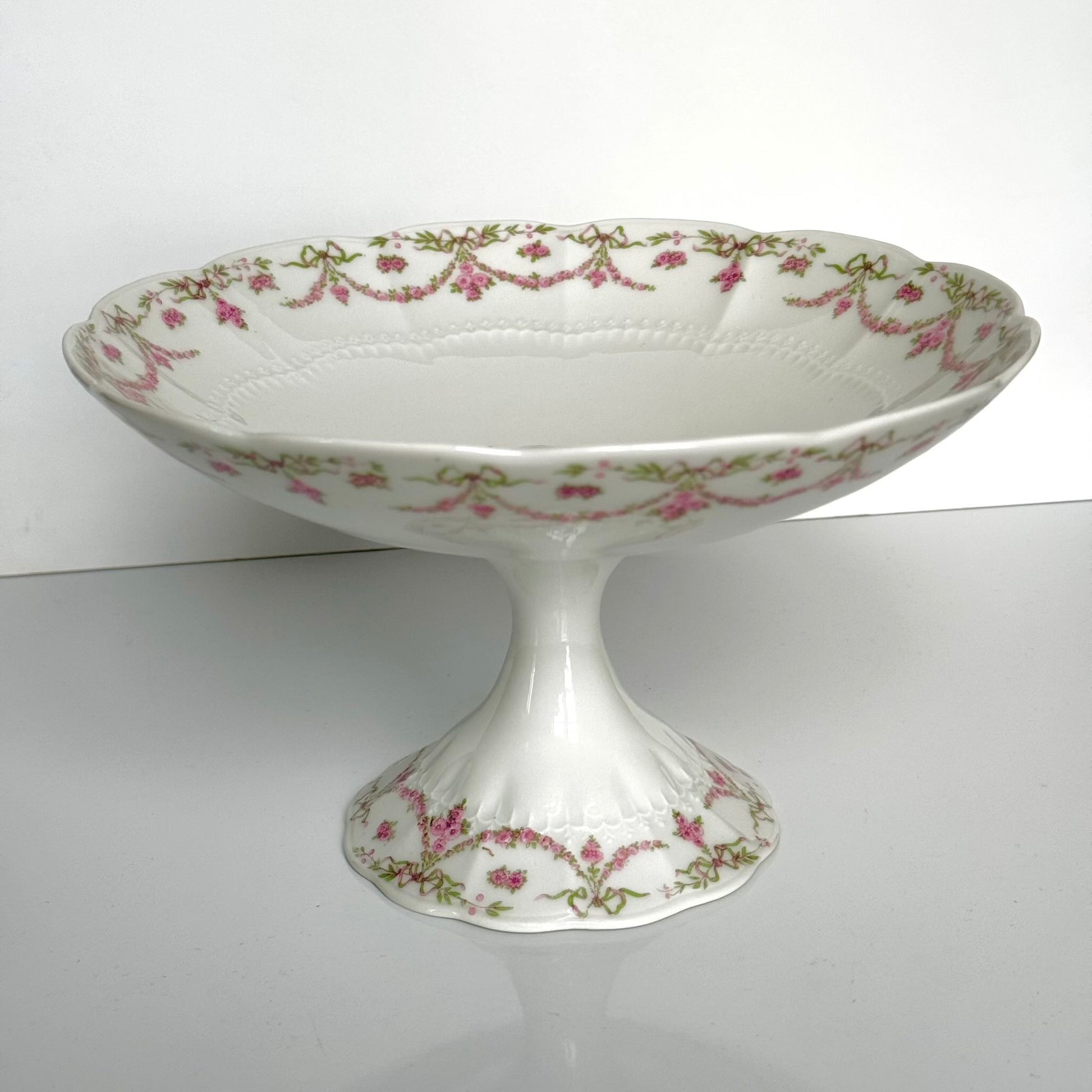 English: Ahrenfeldt Limoges porcelain compote on pedestal with ribbon and floral garland decoration, late 19th to early 20th century, France. ;
Français : Compotier en porcelaine de Limoges Ahrenfeldt sur piédouche, décor de rubans et guirlandes de fleurs, fin XIXᵉ – début XXᵉ siècle. ;
日本語: アーレンフェルト製 リモージュ磁器の脚付きコンポティエ（フルーツスタンド）。リボンとガーランドの装飾、19世紀末〜20世紀初頭 フランス。