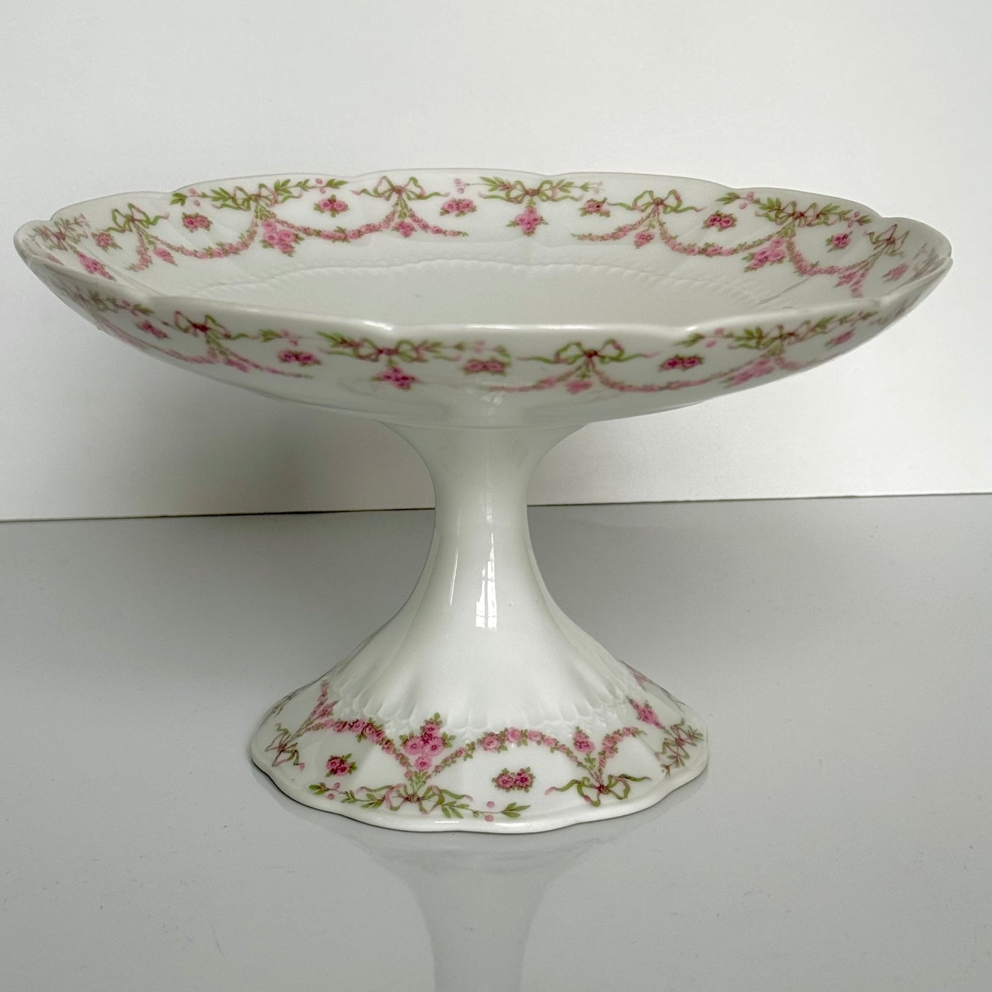 English: Ahrenfeldt Limoges porcelain compote on pedestal with ribbon and floral garland decoration, late 19th to early 20th century, France. ;
Français : Compotier en porcelaine de Limoges Ahrenfeldt sur piédouche, décor de rubans et guirlandes de fleurs, fin XIXᵉ – début XXᵉ siècle. ;
日本語: アーレンフェルト製 リモージュ磁器の脚付きコンポティエ（フルーツスタンド）。リボンとガーランドの装飾、19世紀末〜20世紀初頭 フランス。