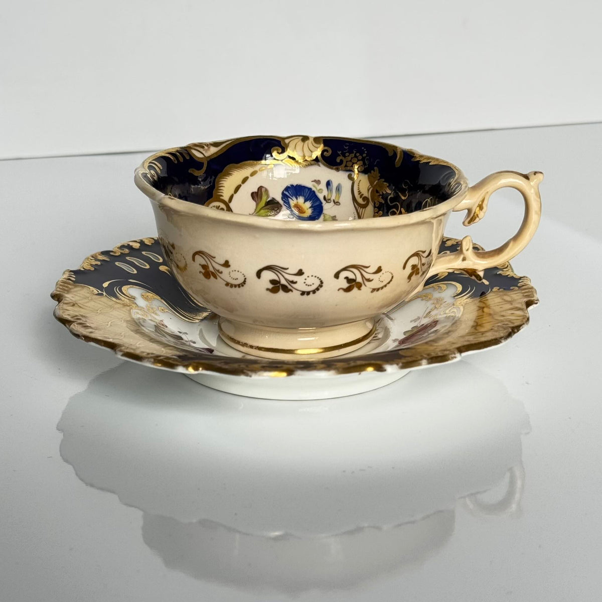 Antique English porcelain teacup and saucer, hand-painted floral and shell decor with heavy gold gilding.