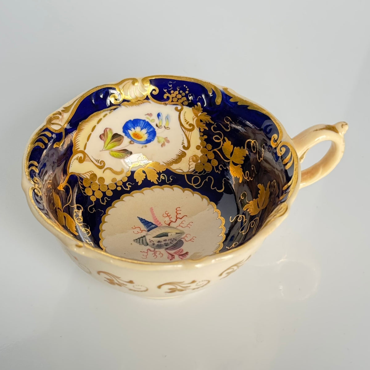 Antique English porcelain teacup and saucer, hand-painted floral and shell decor with heavy gold gilding.