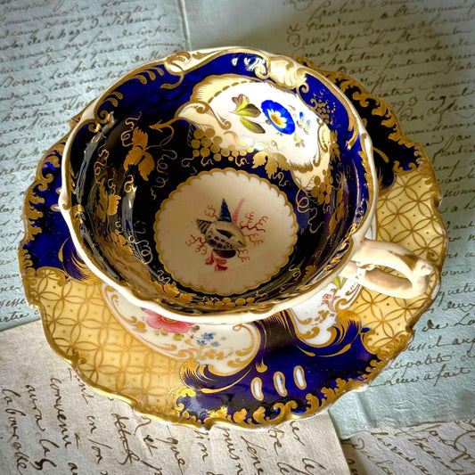 Antique English porcelain teacup and saucer, hand-painted floral and shell decor with heavy gold gilding.