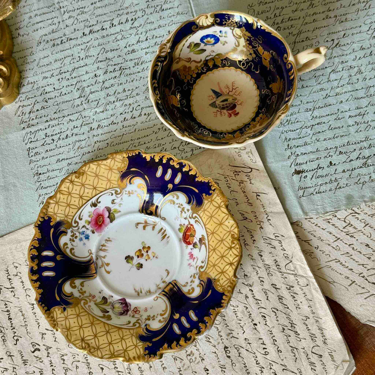 Antique English porcelain teacup and saucer, hand-painted floral and shell decor with heavy gold gilding.