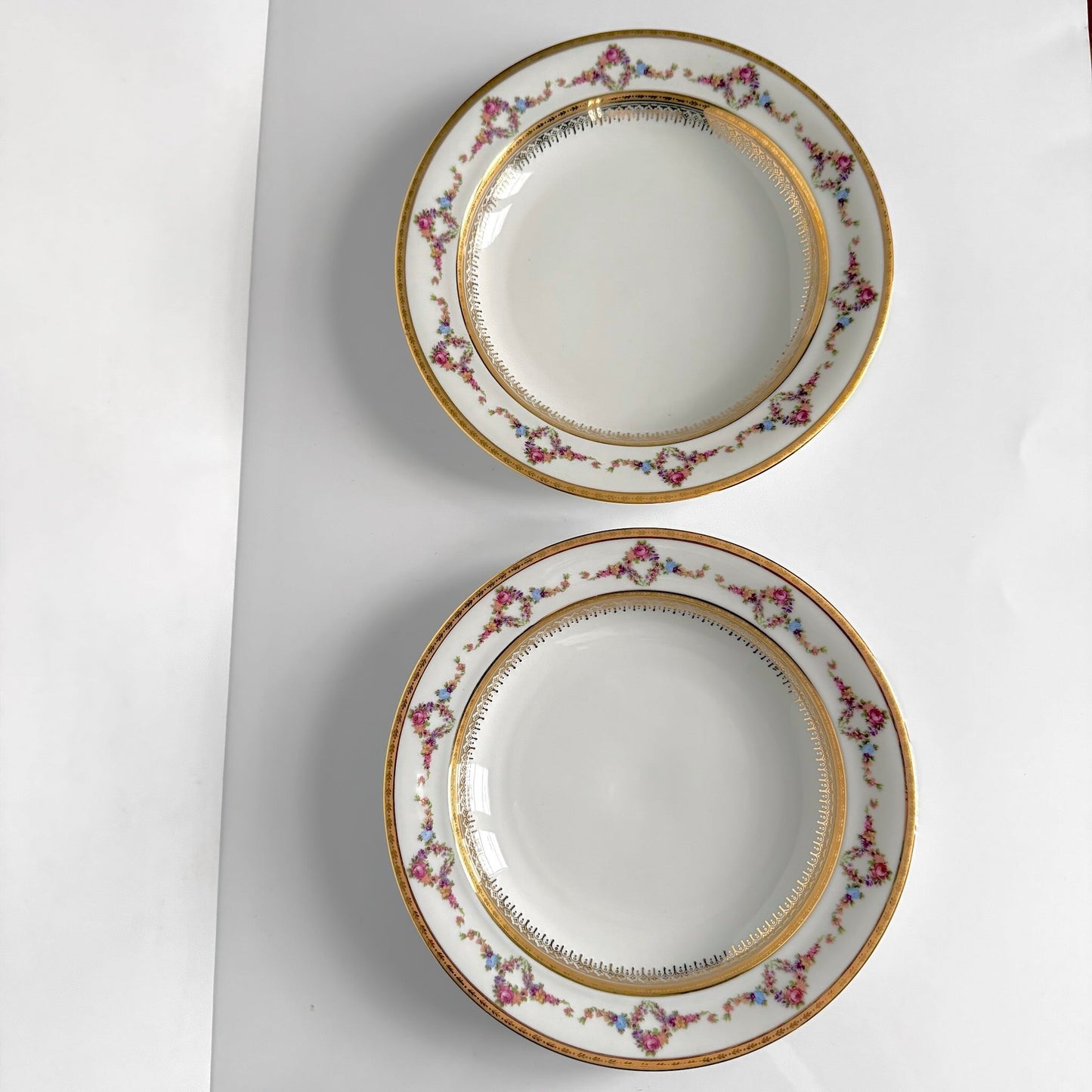 Set of two Limoges P.P. porcelain soup plates featuring floral garlands, wreaths, and rich gilding, 20th century France.