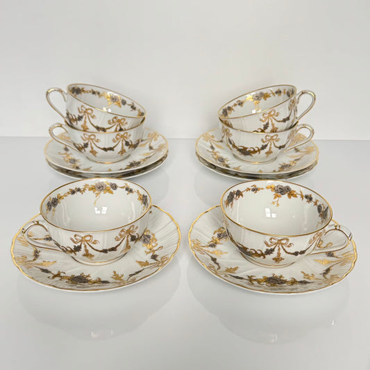 English: Pair of vintage Bernardaud Limoges tea cups and saucers with ribbon and floral garland motif, richly gilded and silvered porcelain set.; 日本語: ベルナルド リモージュ製ヴィンテージ ティーカップ＆ソーサー2客セット、リボンと花のガーランド柄、金彩と銀彩装飾入りの磁器セット。; Français: Paire de tasses à thé et soucoupes vintage Bernardaud Limoges, décor de rubans/nœuds et guirlandes florales, ensemble en porcelaine richement dorée et argentée.