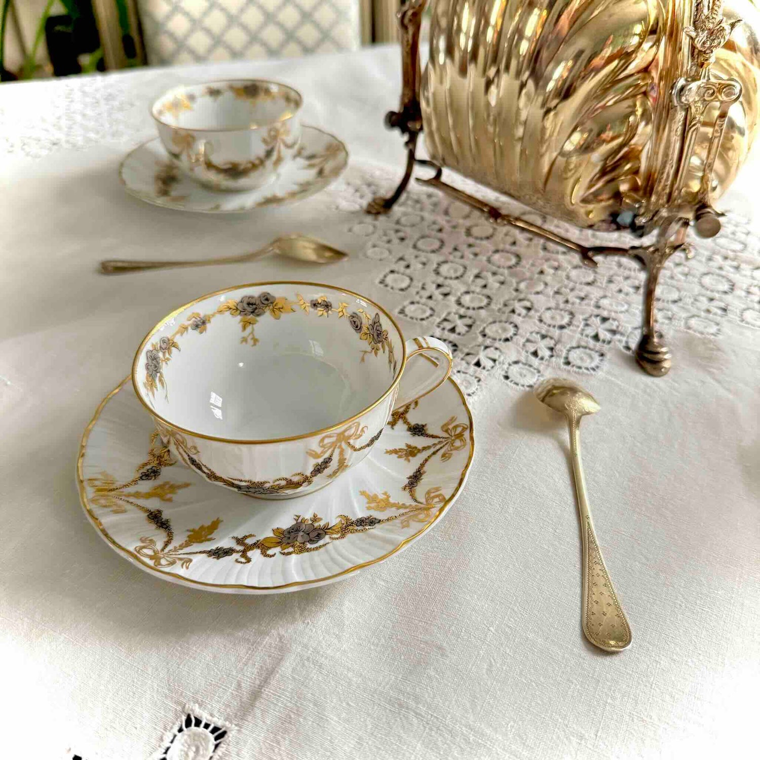 English: Pair of vintage Bernardaud Limoges tea cups and saucers with ribbon and floral garland motif, richly gilded and silvered porcelain set.; 日本語: ベルナルド リモージュ製ヴィンテージ ティーカップ＆ソーサー2客セット、リボンと花のガーランド柄、金彩と銀彩装飾入りの磁器セット。; Français: Paire de tasses à thé et soucoupes vintage Bernardaud Limoges, décor de rubans/nœuds et guirlandes florales, ensemble en porcelaine richement dorée et argentée.