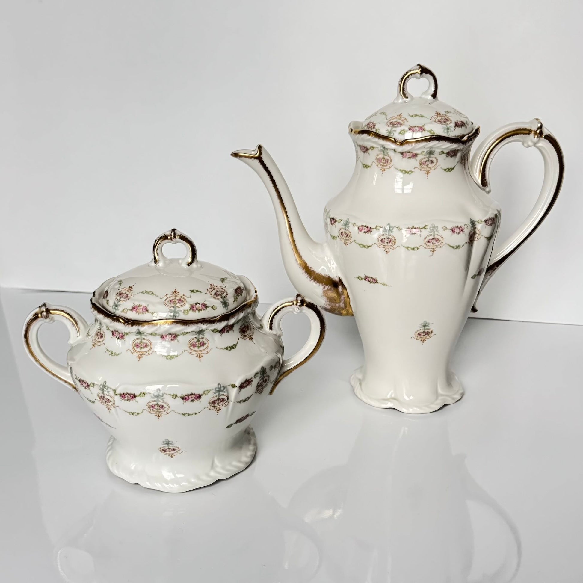 Limoges porcelain tea/coffee pot and sugar pot set with a floral and ribbon design, exuding elegance.