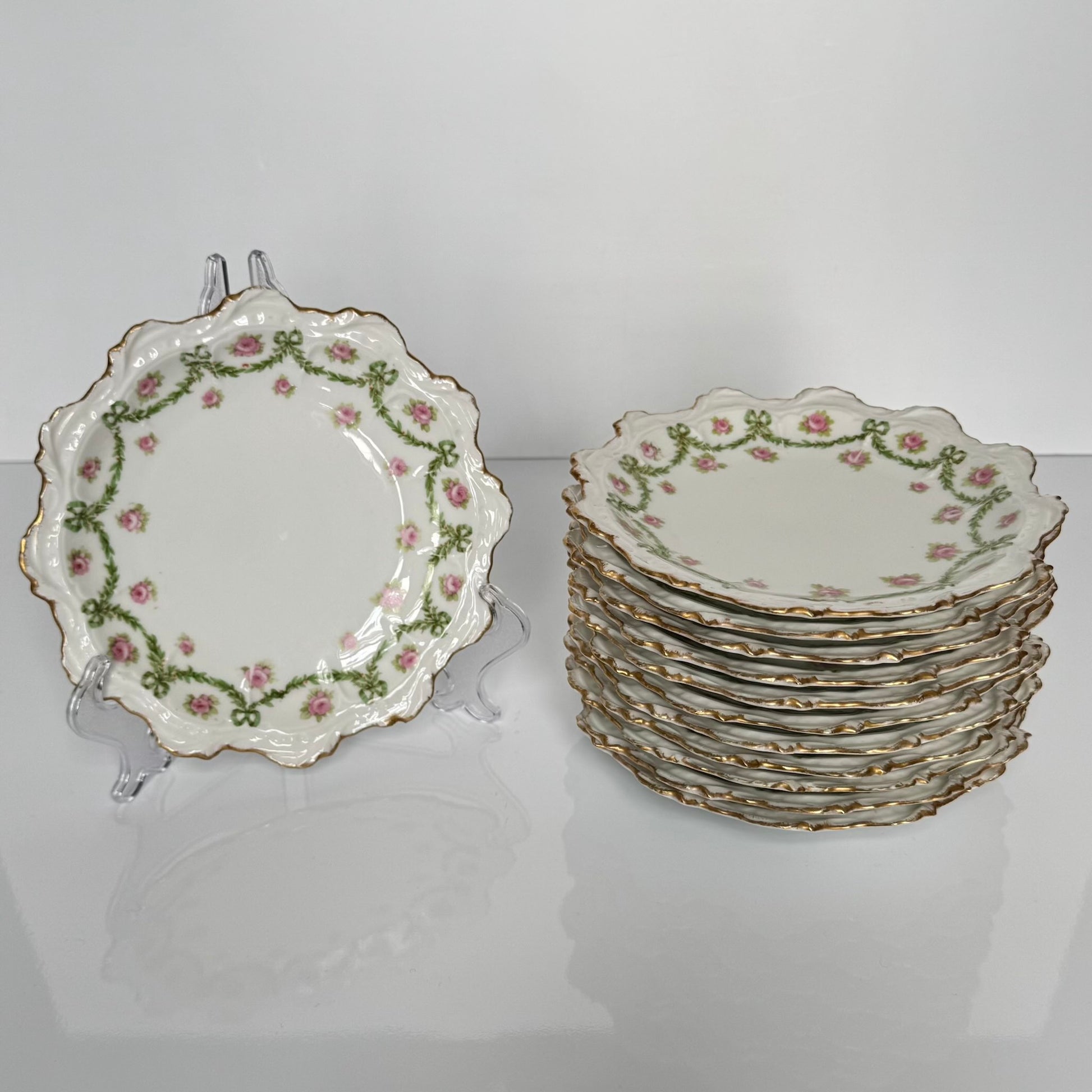 English: Limoges porcelain dessert plate with ribbon and rose motif, early 20th century, subtle gilding. ; Français : Assiette à dessert en porcelaine de Limoges avec décor de rubans et de roses, début XXe siècle, dorure discrète. ; 日本語： リモージュ製のリボンとバラ模様のデザートプレート、20世紀初頭、繊細な金彩入り。