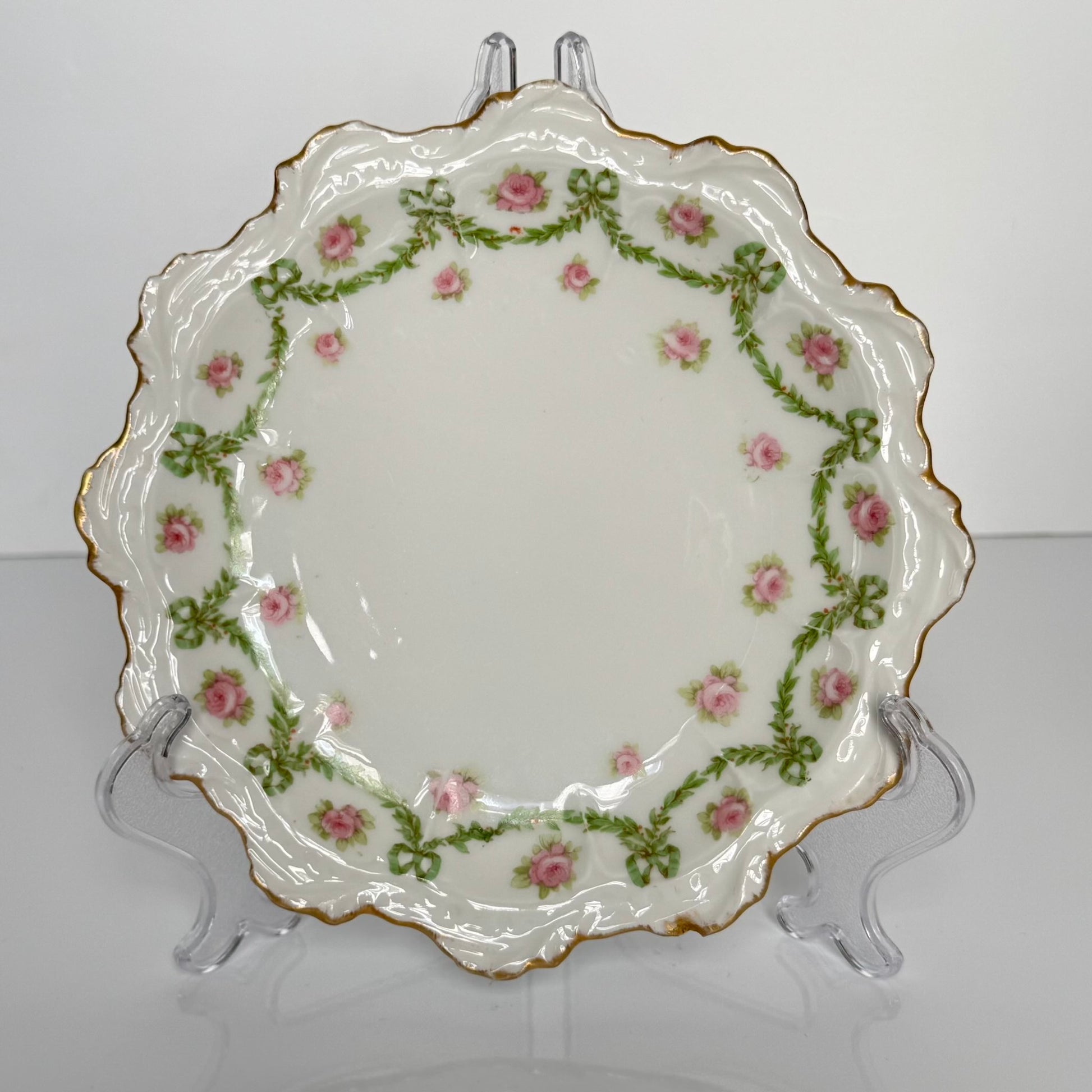English: Limoges porcelain dessert plate with ribbon and rose motif, early 20th century, subtle gilding. ; Français : Assiette à dessert en porcelaine de Limoges avec décor de rubans et de roses, début XXe siècle, dorure discrète. ; 日本語： リモージュ製のリボンとバラ模様のデザートプレート、20世紀初頭、繊細な金彩入り。