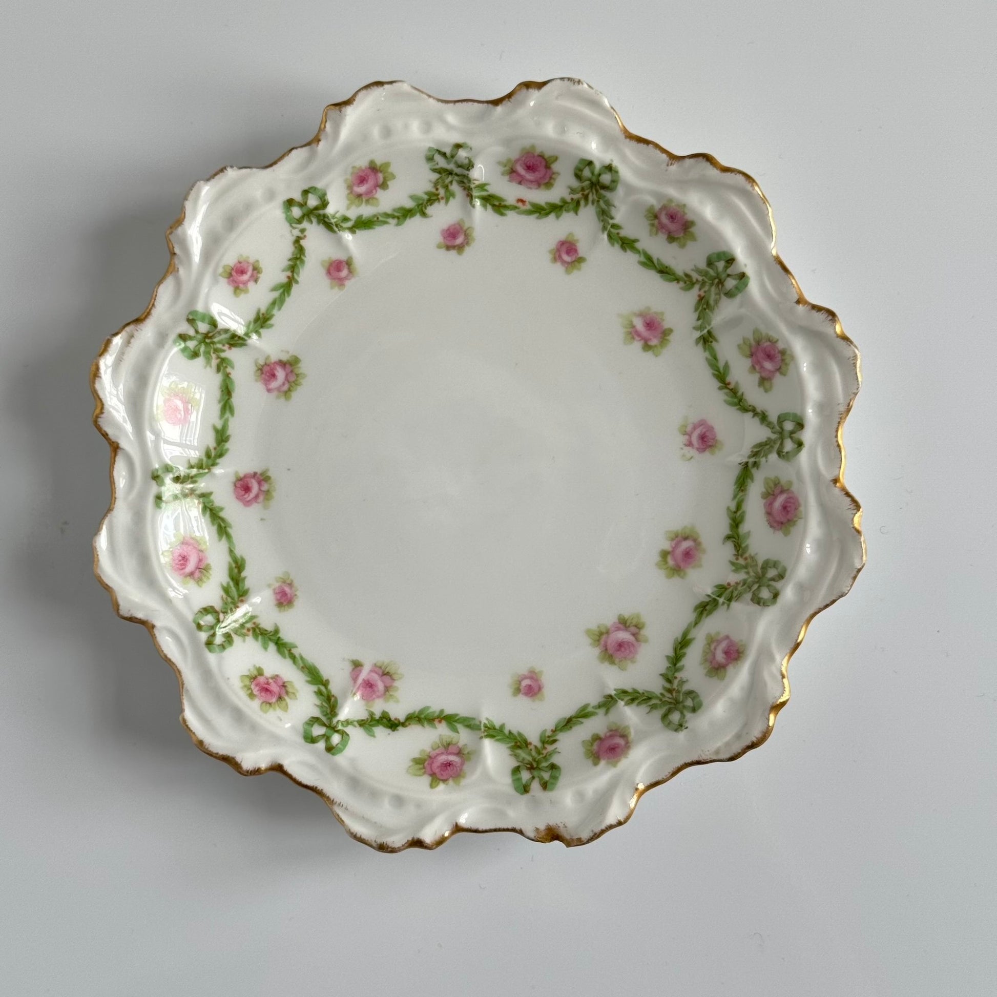 English: Limoges porcelain dessert plate with ribbon and rose motif, early 20th century, subtle gilding. ; Français : Assiette à dessert en porcelaine de Limoges avec décor de rubans et de roses, début XXe siècle, dorure discrète. ; 日本語： リモージュ製のリボンとバラ模様のデザートプレート、20世紀初頭、繊細な金彩入り。
