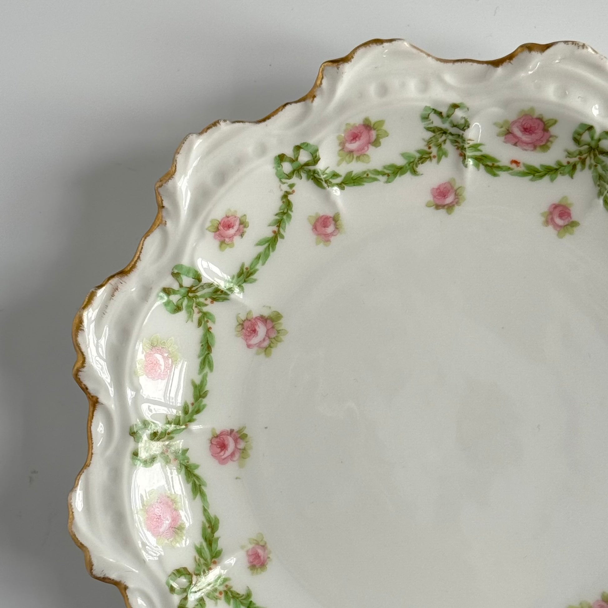 English: Limoges porcelain dessert plate with ribbon and rose motif, early 20th century, subtle gilding. ; Français : Assiette à dessert en porcelaine de Limoges avec décor de rubans et de roses, début XXe siècle, dorure discrète. ; 日本語： リモージュ製のリボンとバラ模様のデザートプレート、20世紀初頭、繊細な金彩入り。