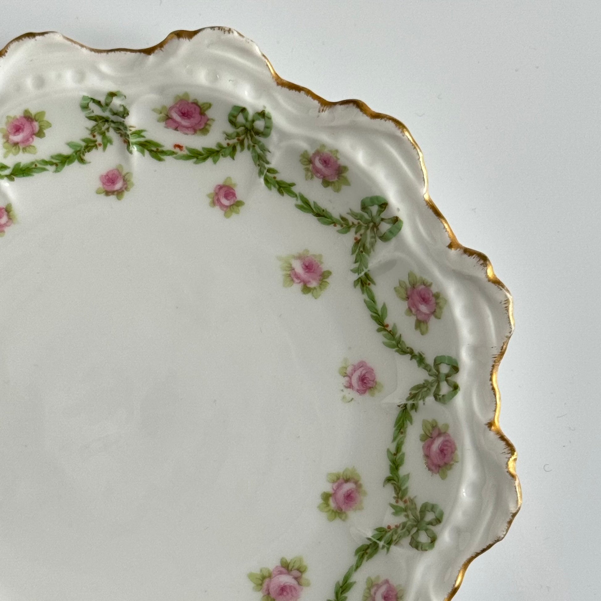 English: Limoges porcelain dessert plate with ribbon and rose motif, early 20th century, subtle gilding. ; Français : Assiette à dessert en porcelaine de Limoges avec décor de rubans et de roses, début XXe siècle, dorure discrète. ; 日本語： リモージュ製のリボンとバラ模様のデザートプレート、20世紀初頭、繊細な金彩入り。
