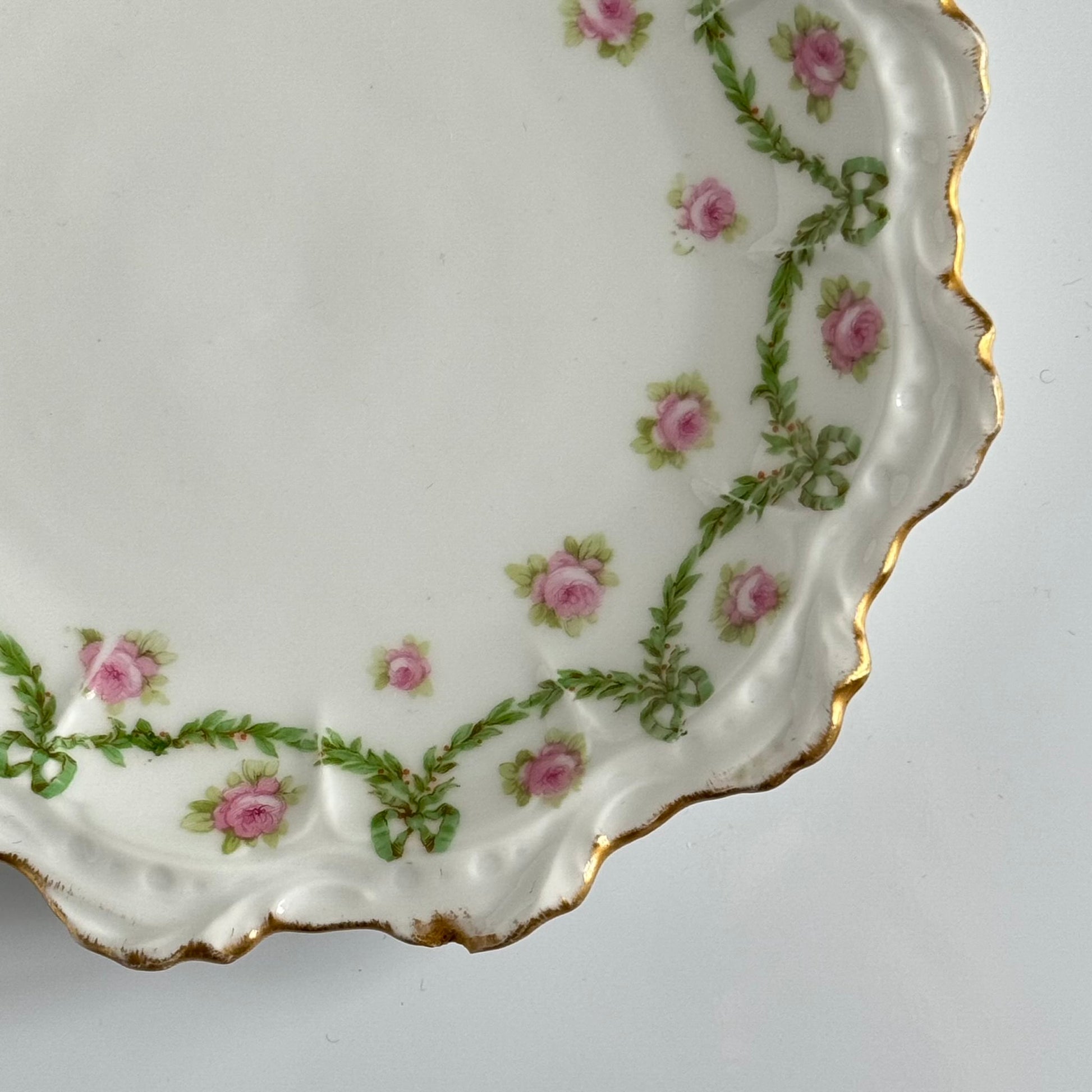 English: Limoges porcelain dessert plate with ribbon and rose motif, early 20th century, subtle gilding. ; Français : Assiette à dessert en porcelaine de Limoges avec décor de rubans et de roses, début XXe siècle, dorure discrète. ; 日本語： リモージュ製のリボンとバラ模様のデザートプレート、20世紀初頭、繊細な金彩入り。