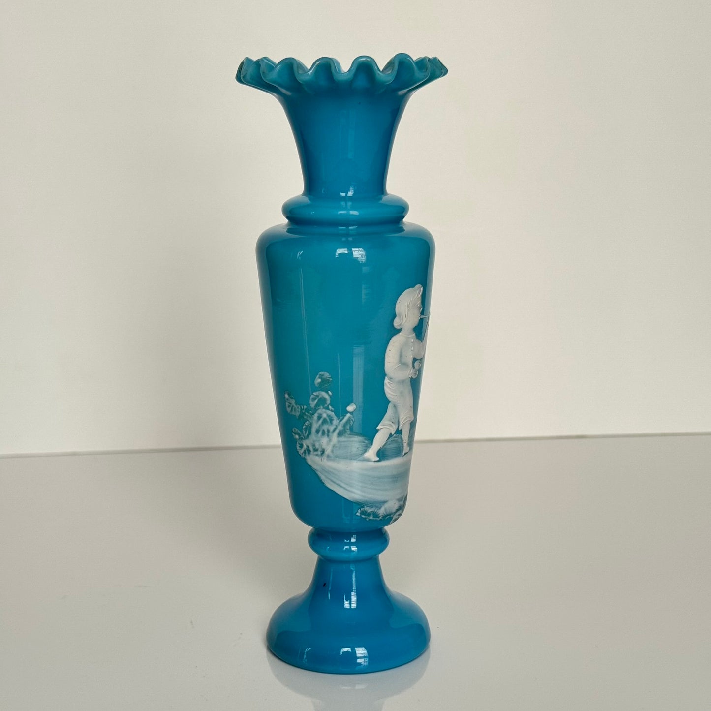 English: Blue opaline glass vase in Mary Gregory style, depicting a Victorian child blowing bubbles, hand-painted white enamel design; 日本語: メアリー・グレゴリー風の青いオパリンガラスの花瓶、シャボン玉を吹くヴィクトリア時代の子供を描いた手描き白エナメル装飾; Français: Vase en verre opalin bleu dans le style de Mary Gregory, décoré d’un enfant victorien soufflant des bulles, émaillé blanc peint à la main.