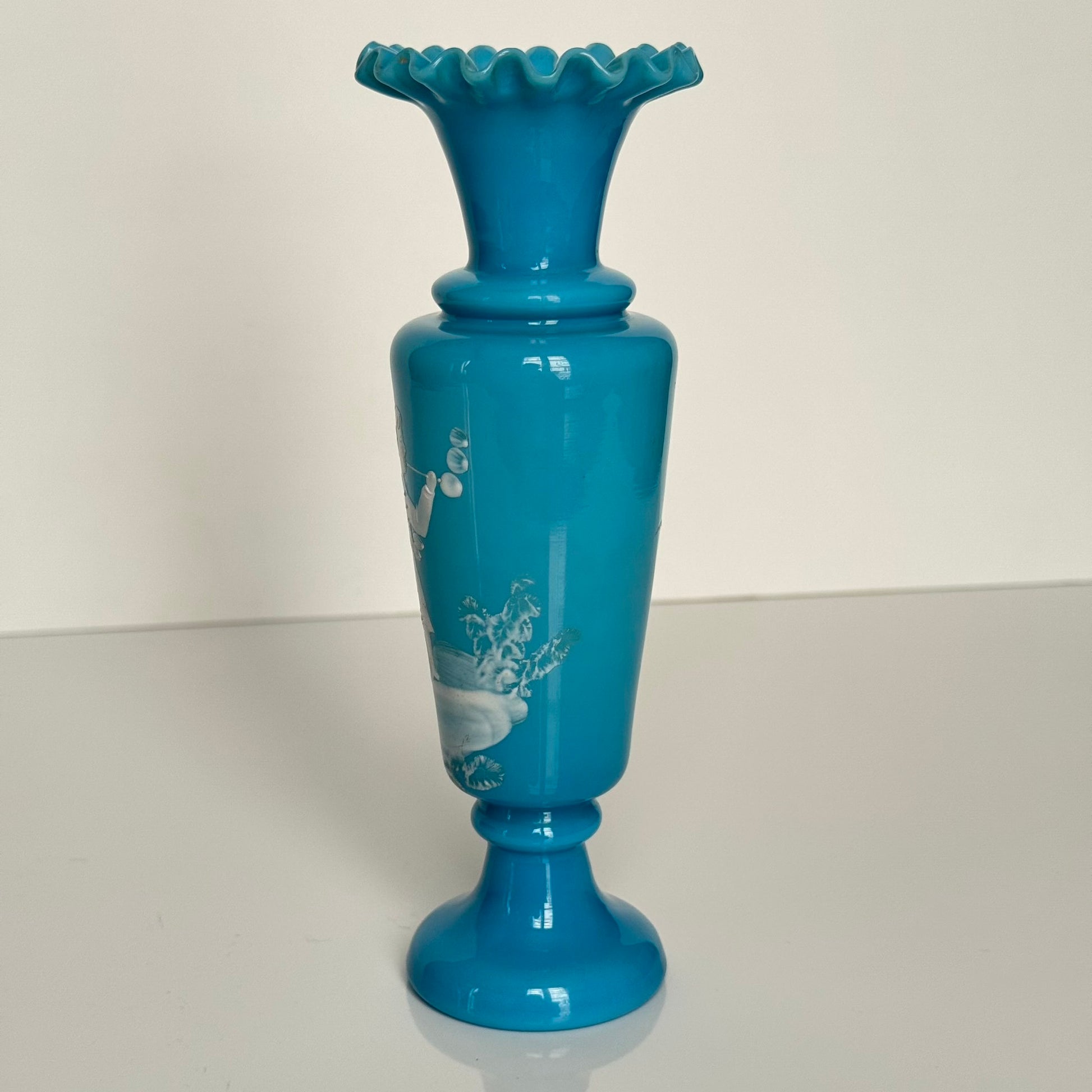 English: Blue opaline glass vase in Mary Gregory style, depicting a Victorian child blowing bubbles, hand-painted white enamel design; 日本語: メアリー・グレゴリー風の青いオパリンガラスの花瓶、シャボン玉を吹くヴィクトリア時代の子供を描いた手描き白エナメル装飾; Français: Vase en verre opalin bleu dans le style de Mary Gregory, décoré d’un enfant victorien soufflant des bulles, émaillé blanc peint à la main.