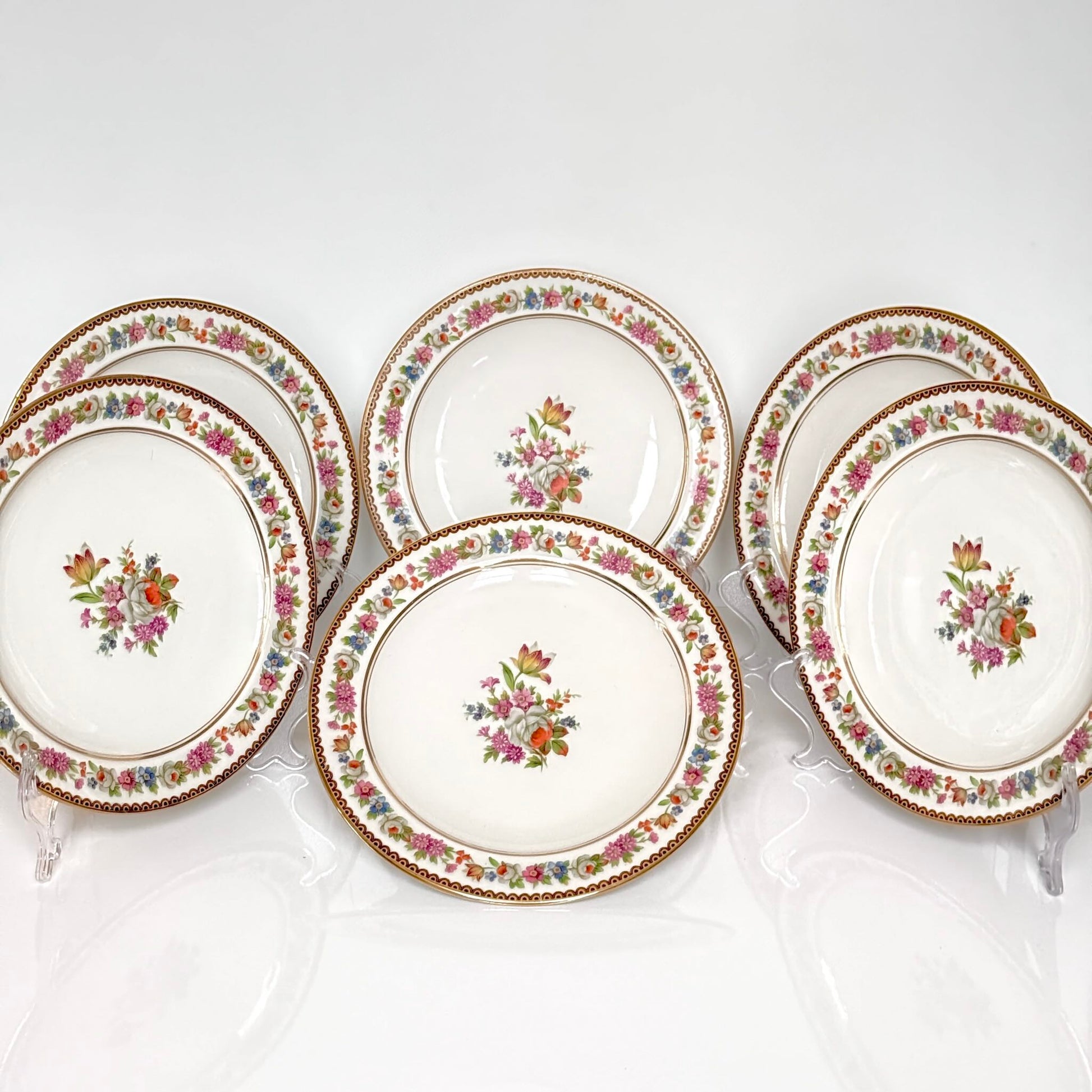 Raynaud Limoges floral porcelain dessert plates, set of two, early 20th century, featuring a central flower bouquet, floral garland border, and triple gilded rims.